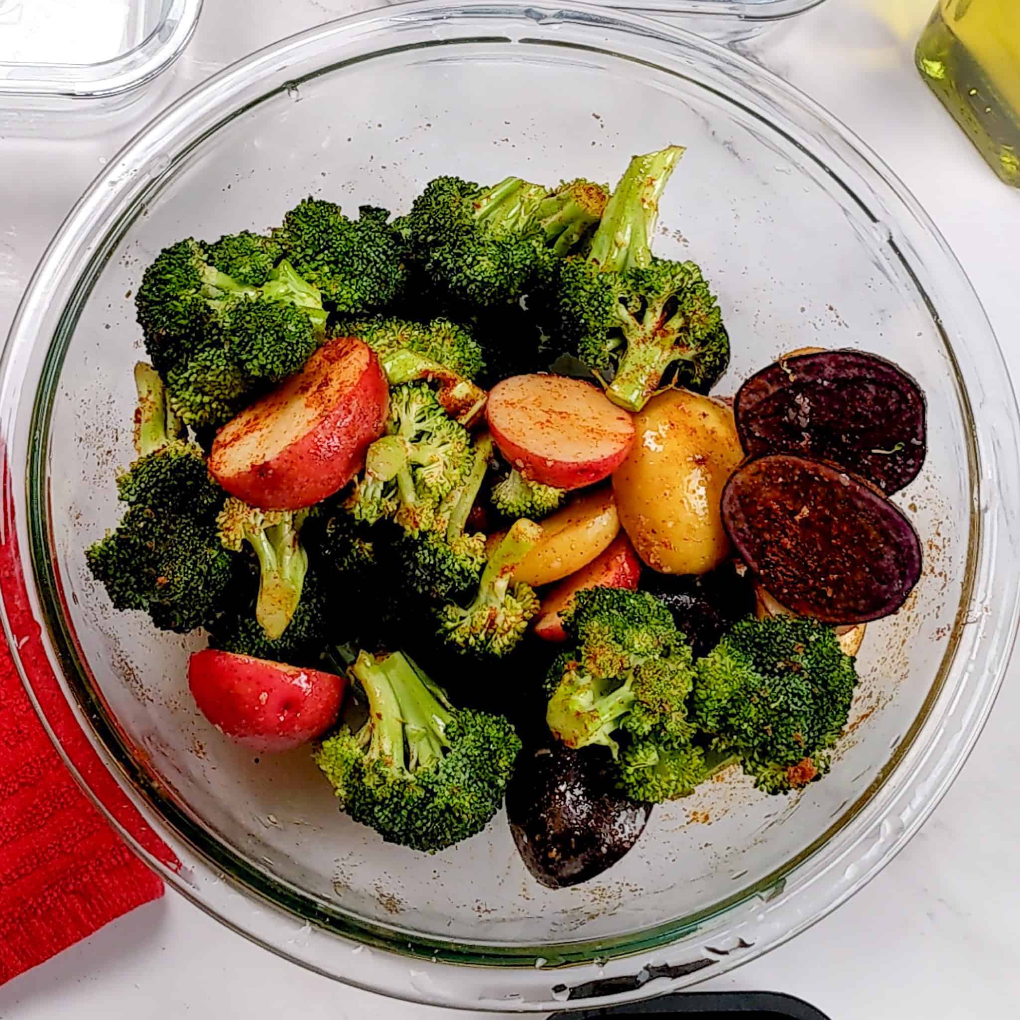 seasoned halved medley baby potatoes and broccoli florets in a glass mixing bowl.