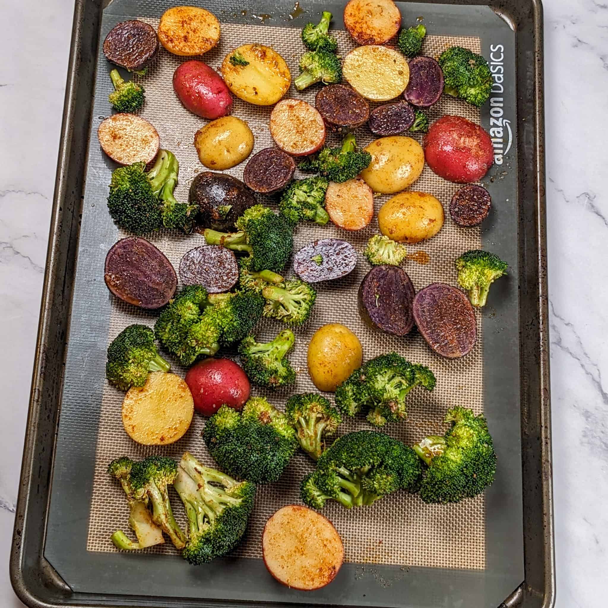 seasoned broccoli florets and halved baby medley potatoes on a silicone lined sheet pan.