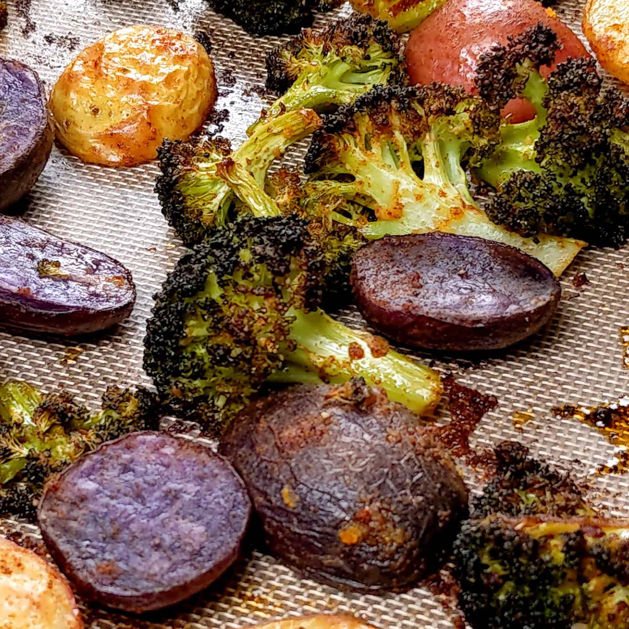 roasted halved medley baby potatoes and broccoli florets on a silicone liner lined sheet pan.