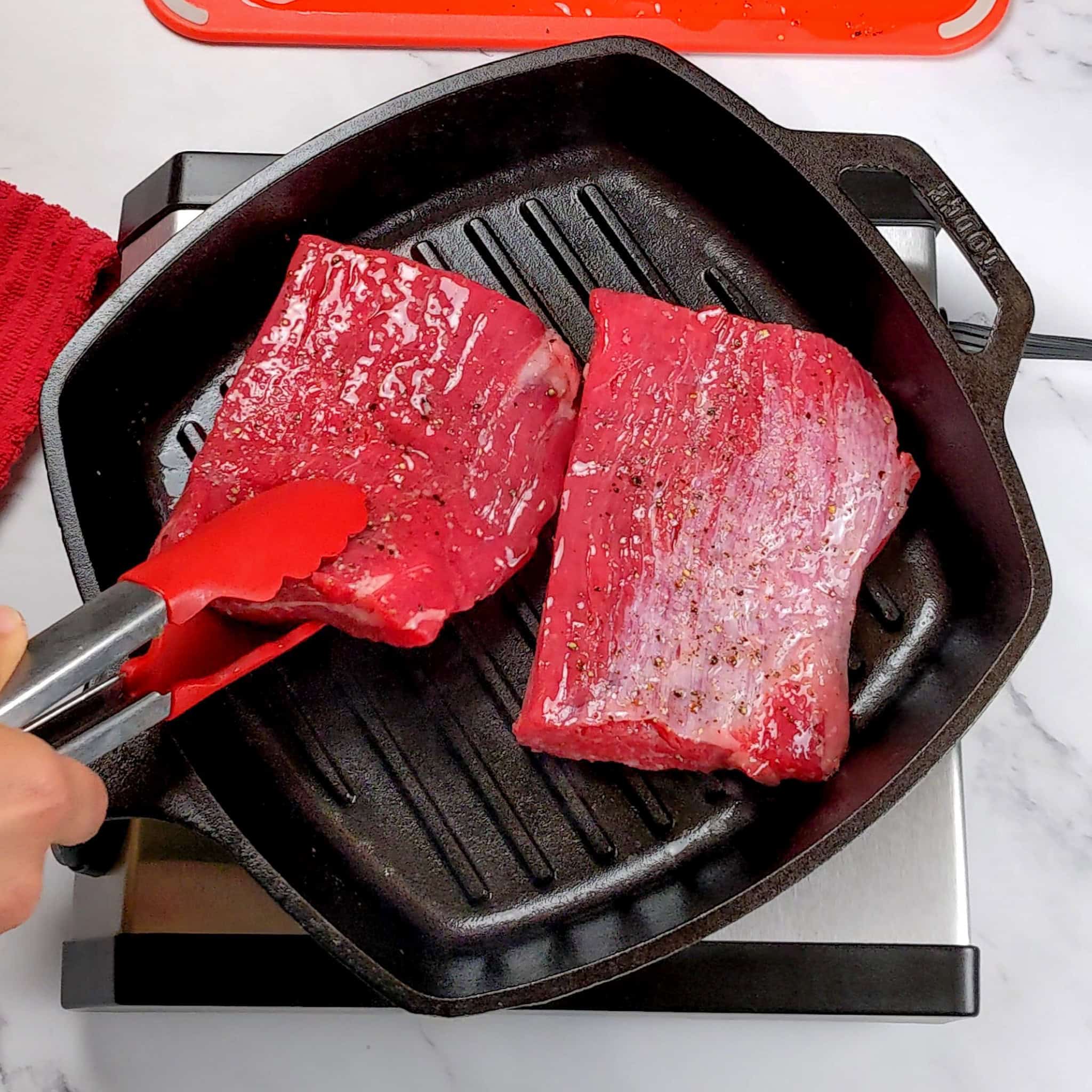 raw portioned and seasoned flank steak in a grill pan.