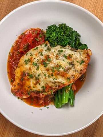 Baked Cheesy Spicy Tomato Basil Chicken and Broccolini on a wide rim bowl.