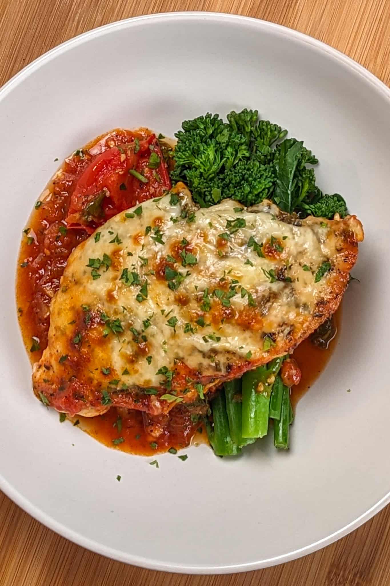 Baked Cheesy Spicy Tomato Basil Chicken and Broccolini on a wide rim bowl.