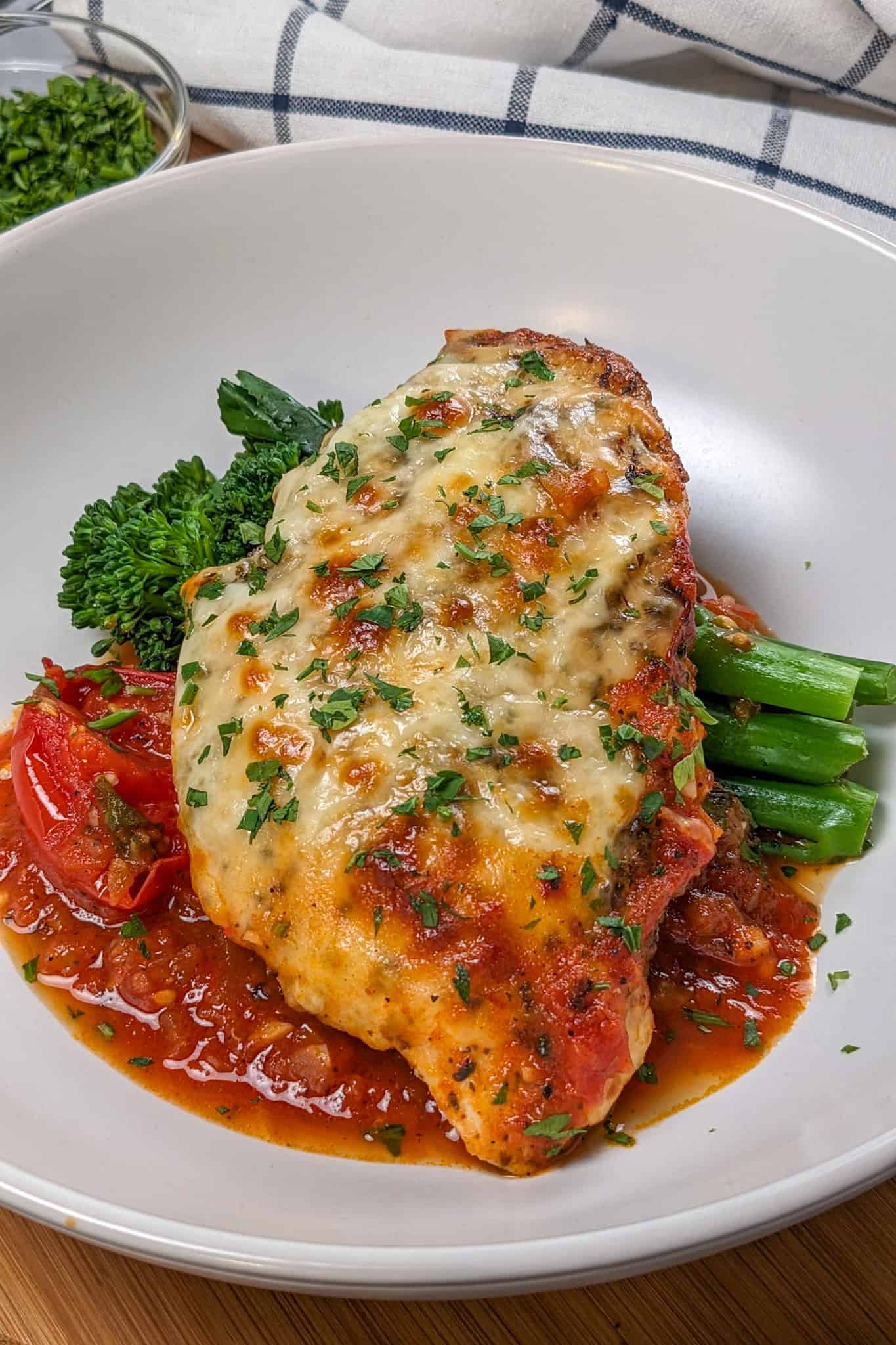 Baked Cheesy Spicy Tomato Basil Chicken and Broccolini on a wide rim bowl.