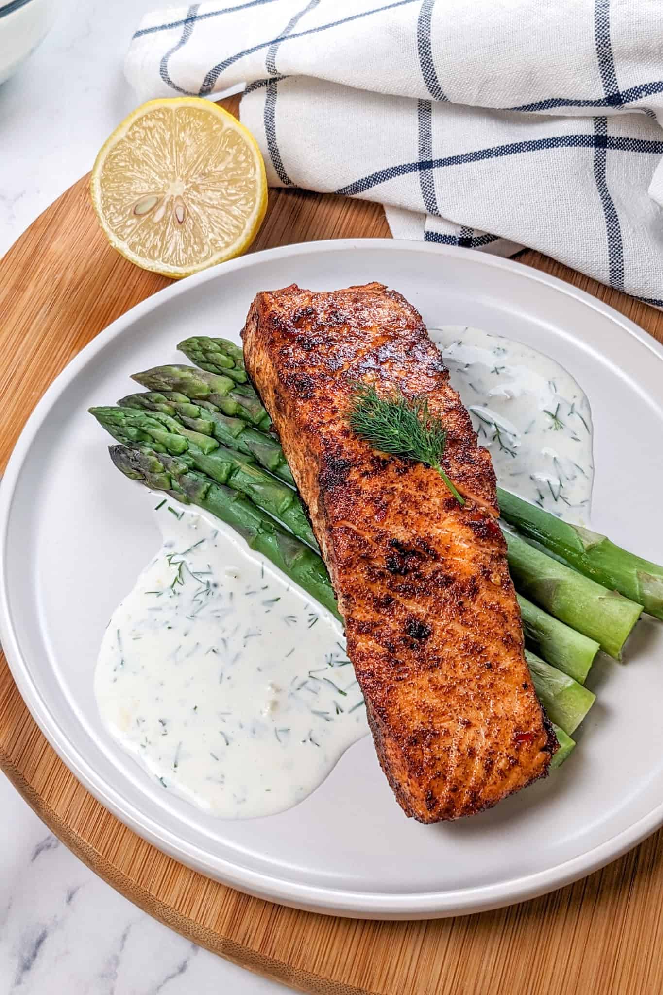 smoked paprika Calabrian Pepper marinated pan-seared Salmon with Creamy Lemon Dill Sauce and jumbo asparagus on a round white plate.