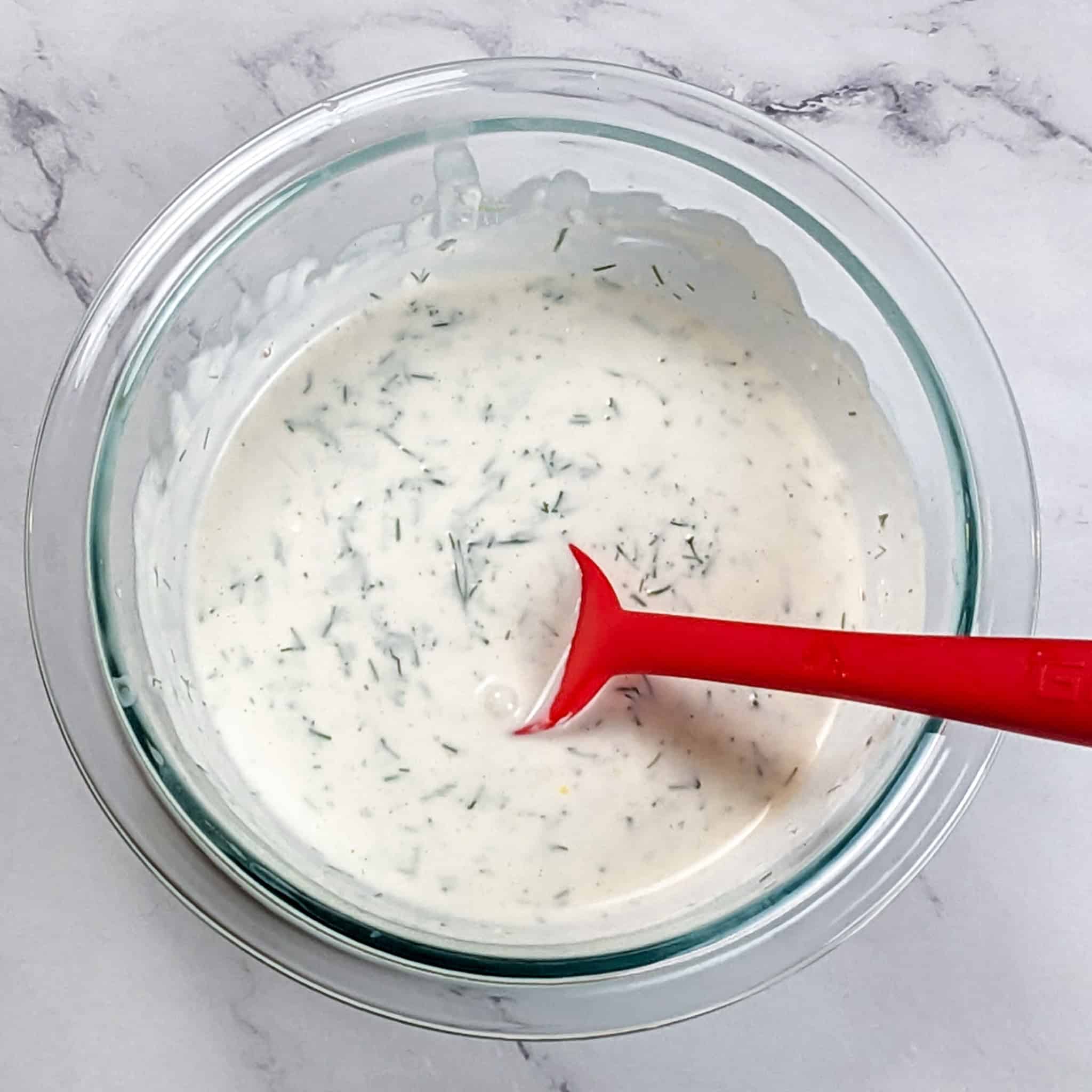 lemon dill sauce in a glass mixing bowl with a silicone spoon sitting in it.