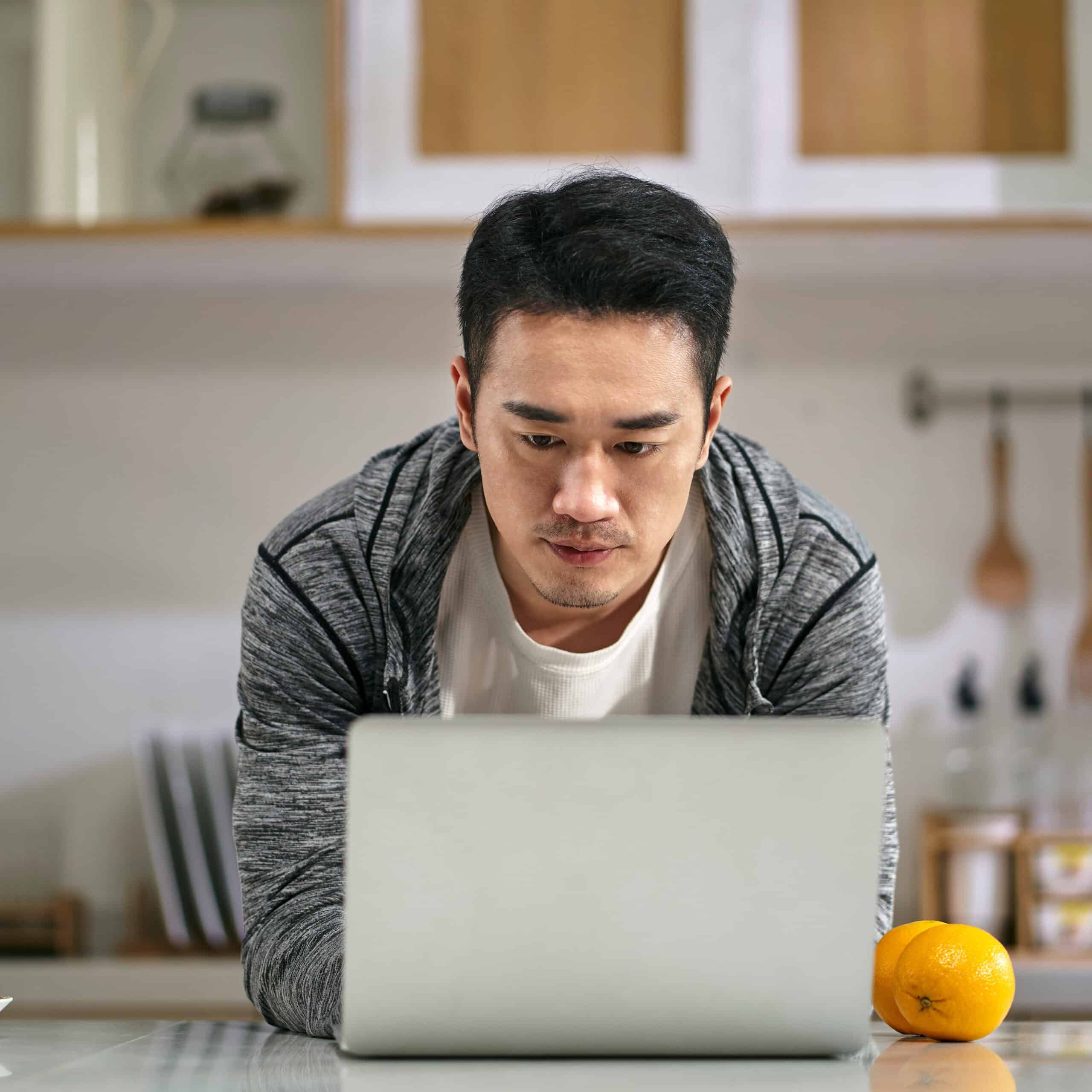 young asian business man working in kitchen at home using laptop computer