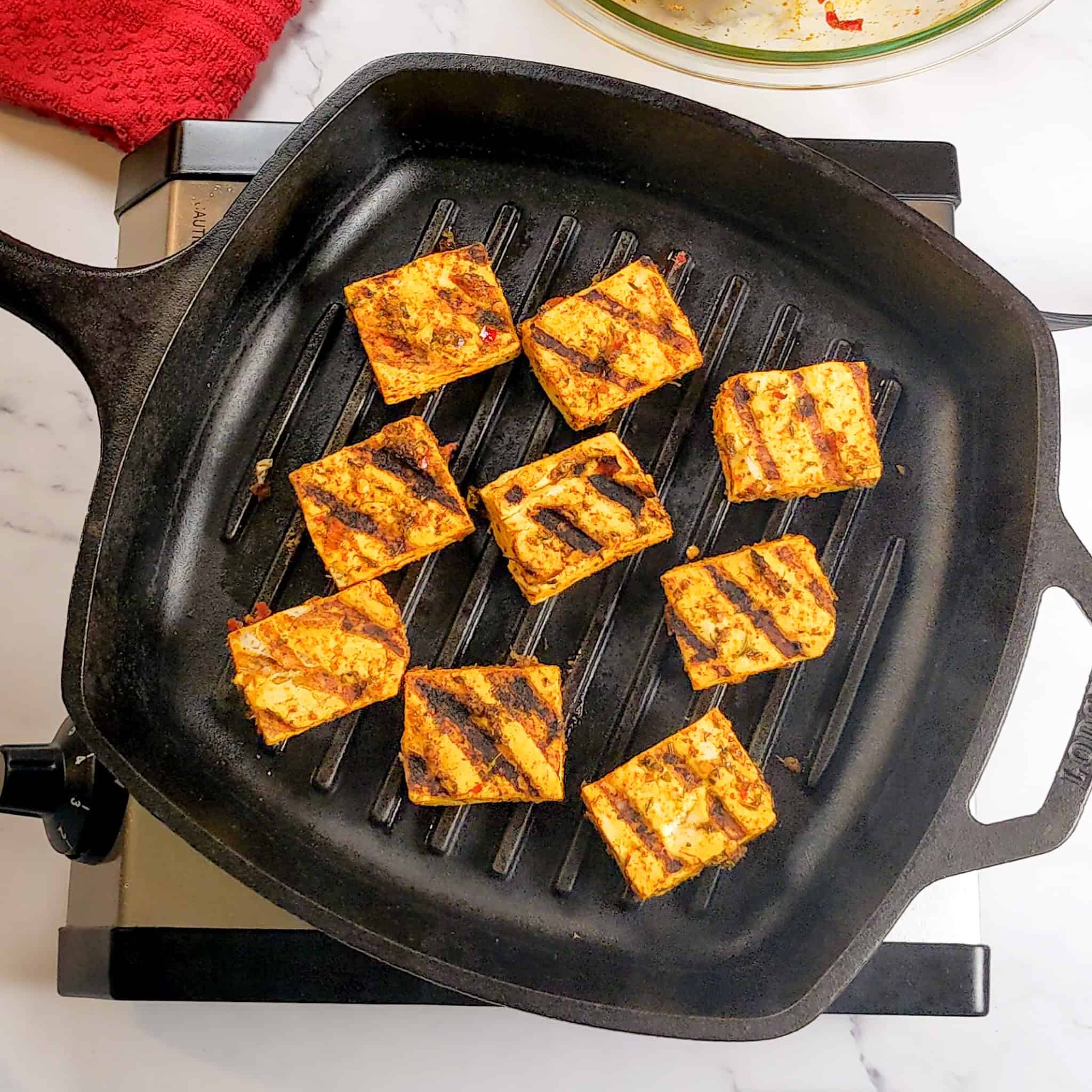 marinated tofu grilling in a grill pan, flipped and showing grill marks.