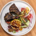 Grilled Zhug Ras el Hanout Lamb Chops and Tomato, cucumber, onion Salad served with a lemon-oregano dressing served with a grilled lemon.
