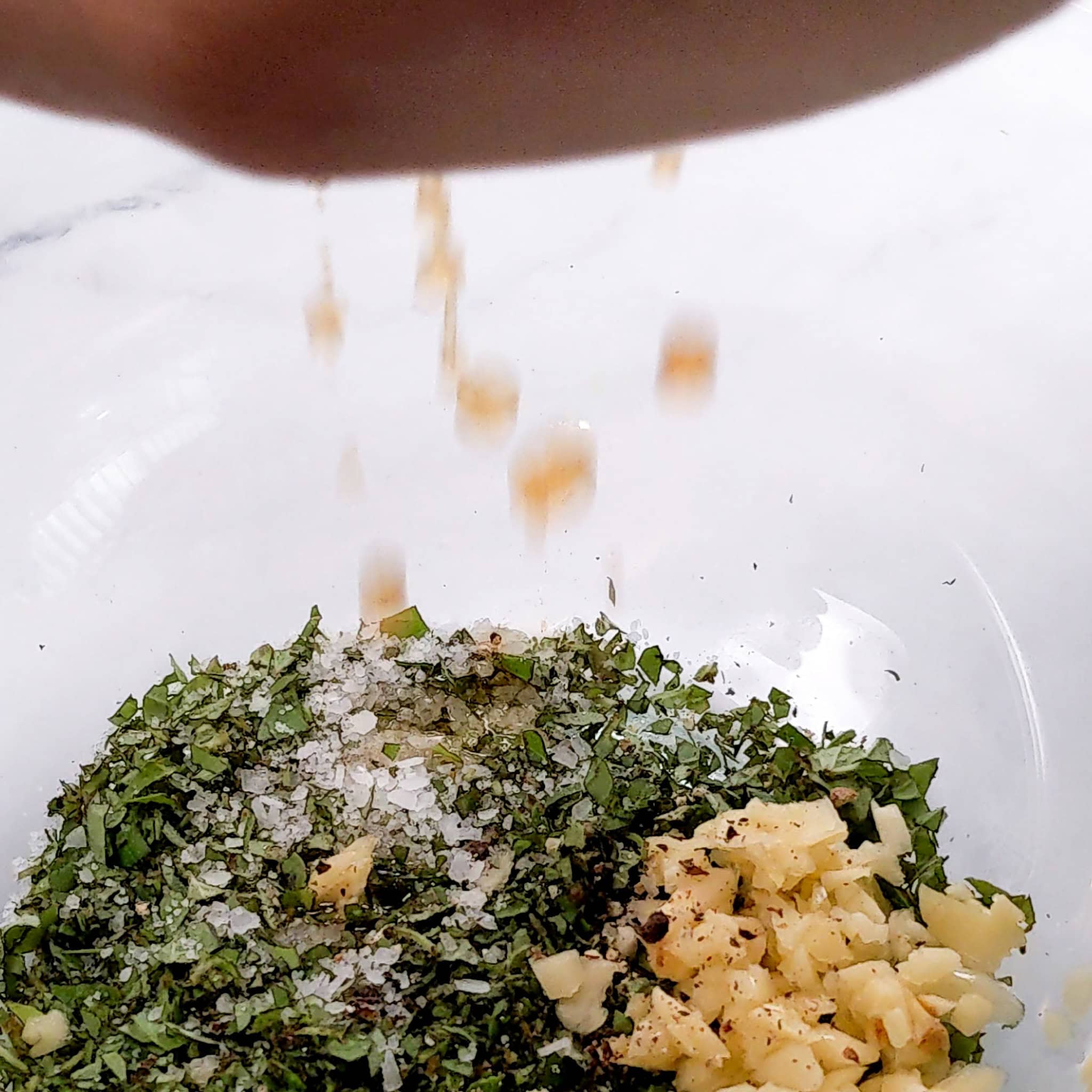 lemon juice being squeezed into the bowl of ingredients for the lemon oregano vinaigrette.