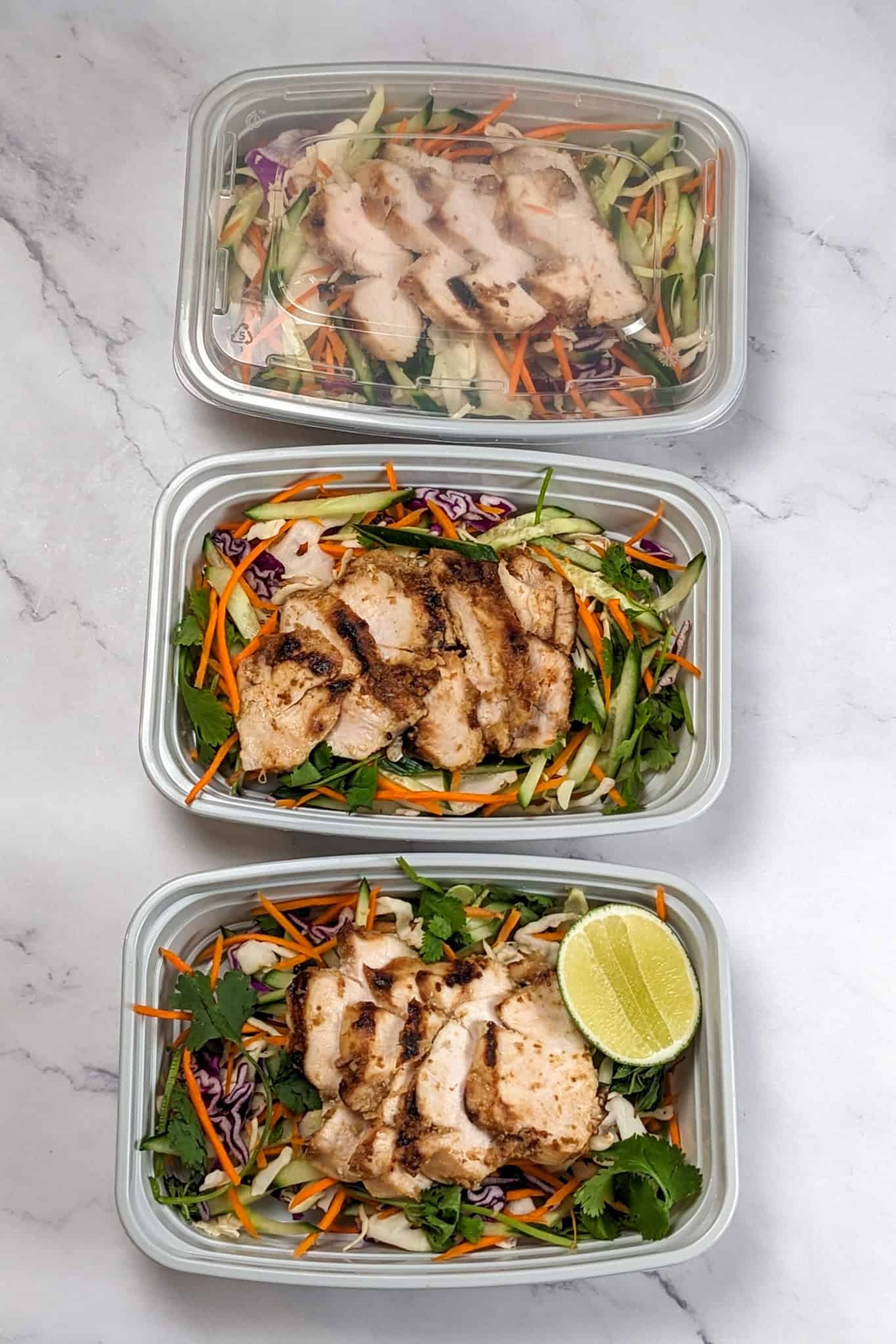 the recipe's sliced chicken and salad in meal prep containers.