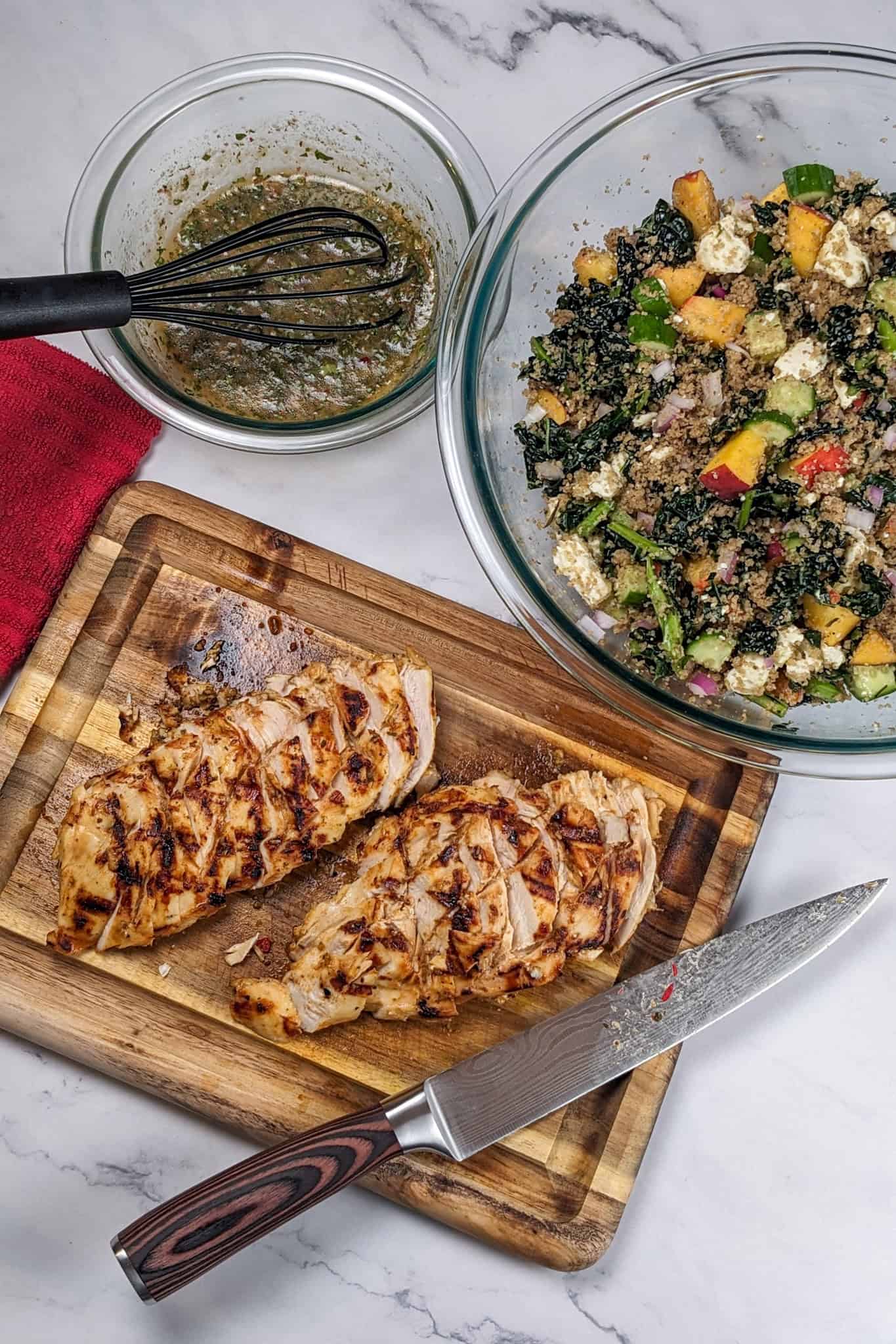 grilled and sliced peach piri piri marinated chicken on a wooden cutting board, peach vinaigrette and a fonio peach cucumber salad.