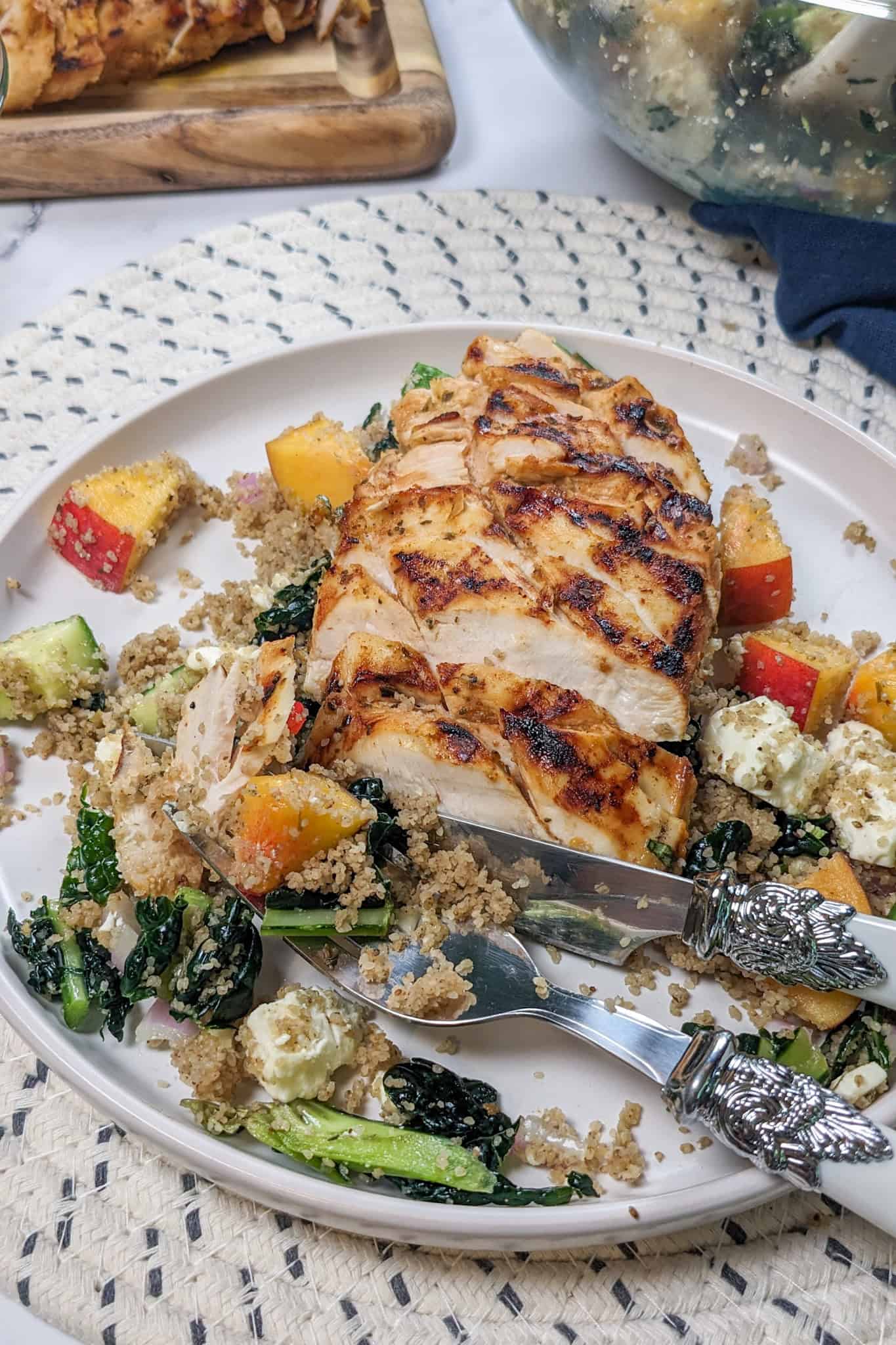 Sliced Peach Piri Piri Chicken with Fonio Kale Salad on a plate being eaten with a fork and knife.