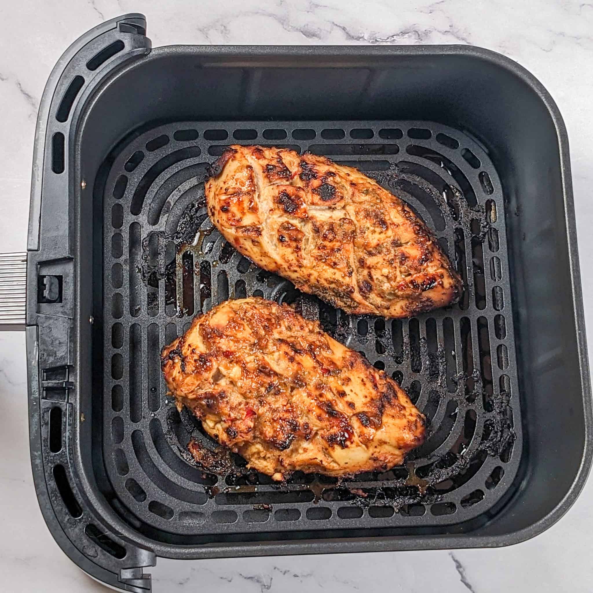 cooked peach piri piri marinated chicken in an air fryer basket.