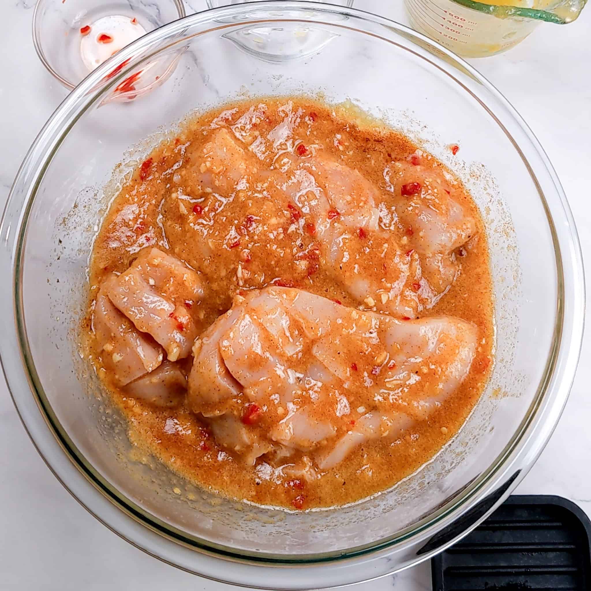 peach piri piri chicken marinating in a glass mixing bowl.