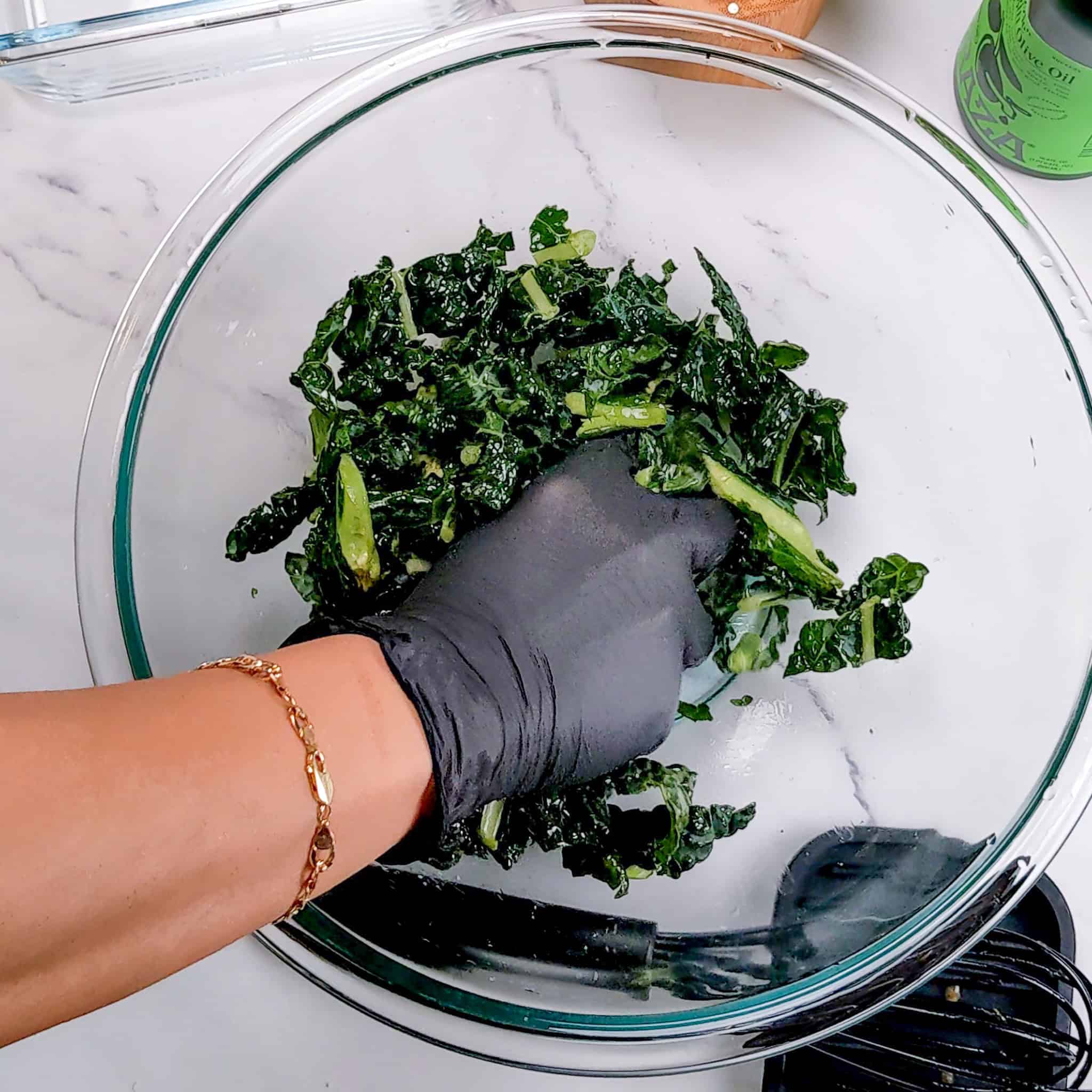 kale being massaged in a glass mixing bowl.