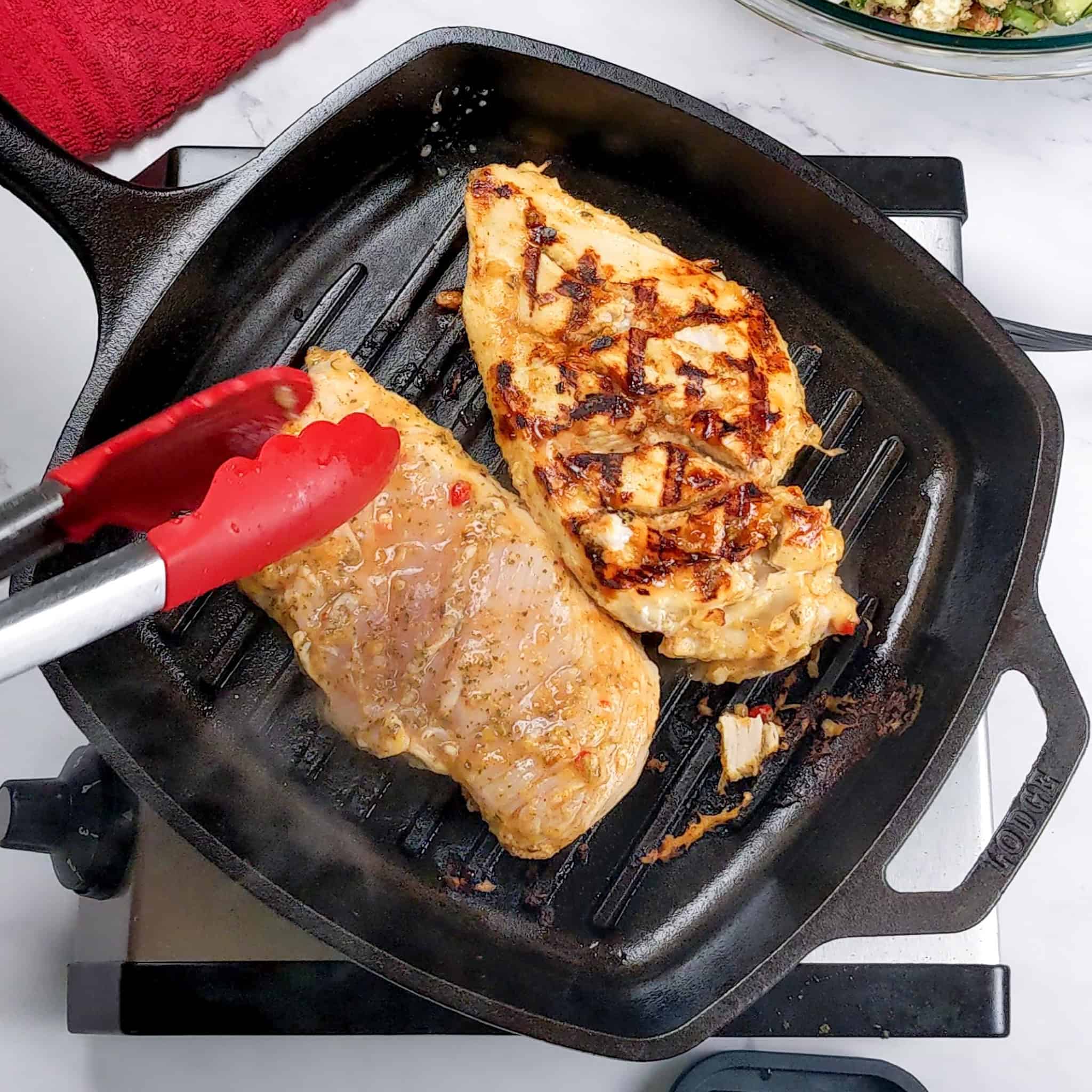 grilled marinated chicken breast grilling in a lodge cast iron grill pan.