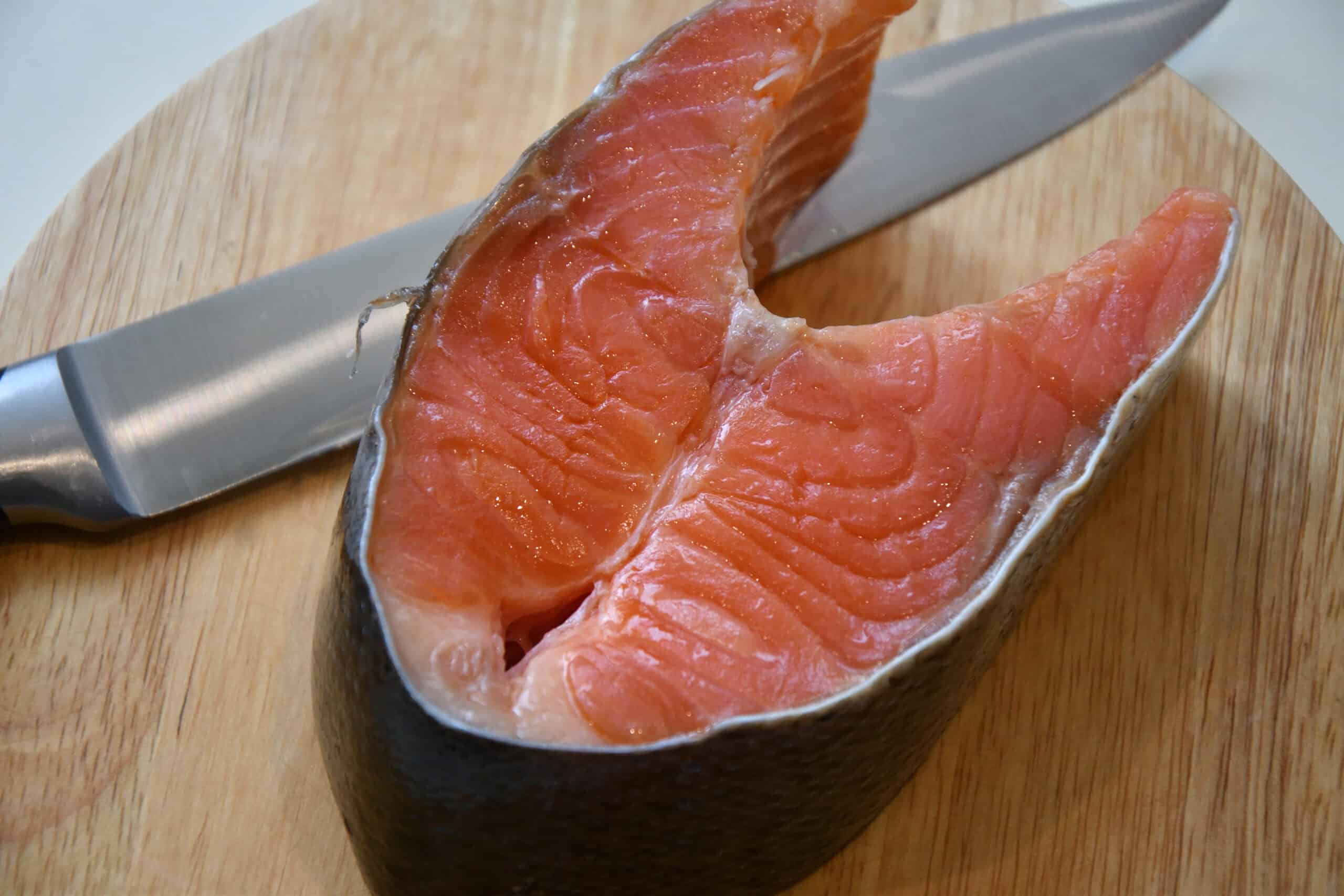 a king salmon filet on a round wooden cutting board next to a carving knife.