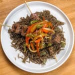 Grilled beef skewers with black mushroom rice on a flat round plate.