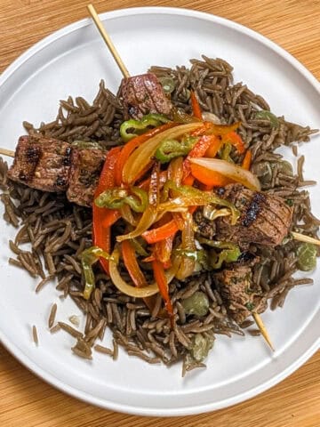 Grilled beef skewers with black mushroom rice on a flat round plate.