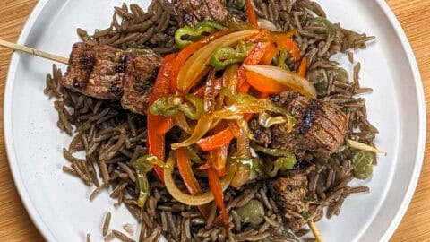 Grilled beef skewers with black mushroom rice on a flat round plate.