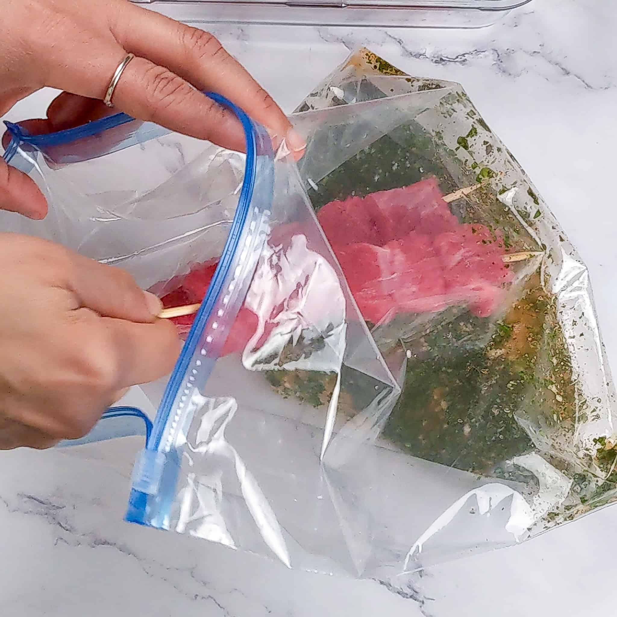 Raw beef skewers are placed in a resealable bag with marinade.