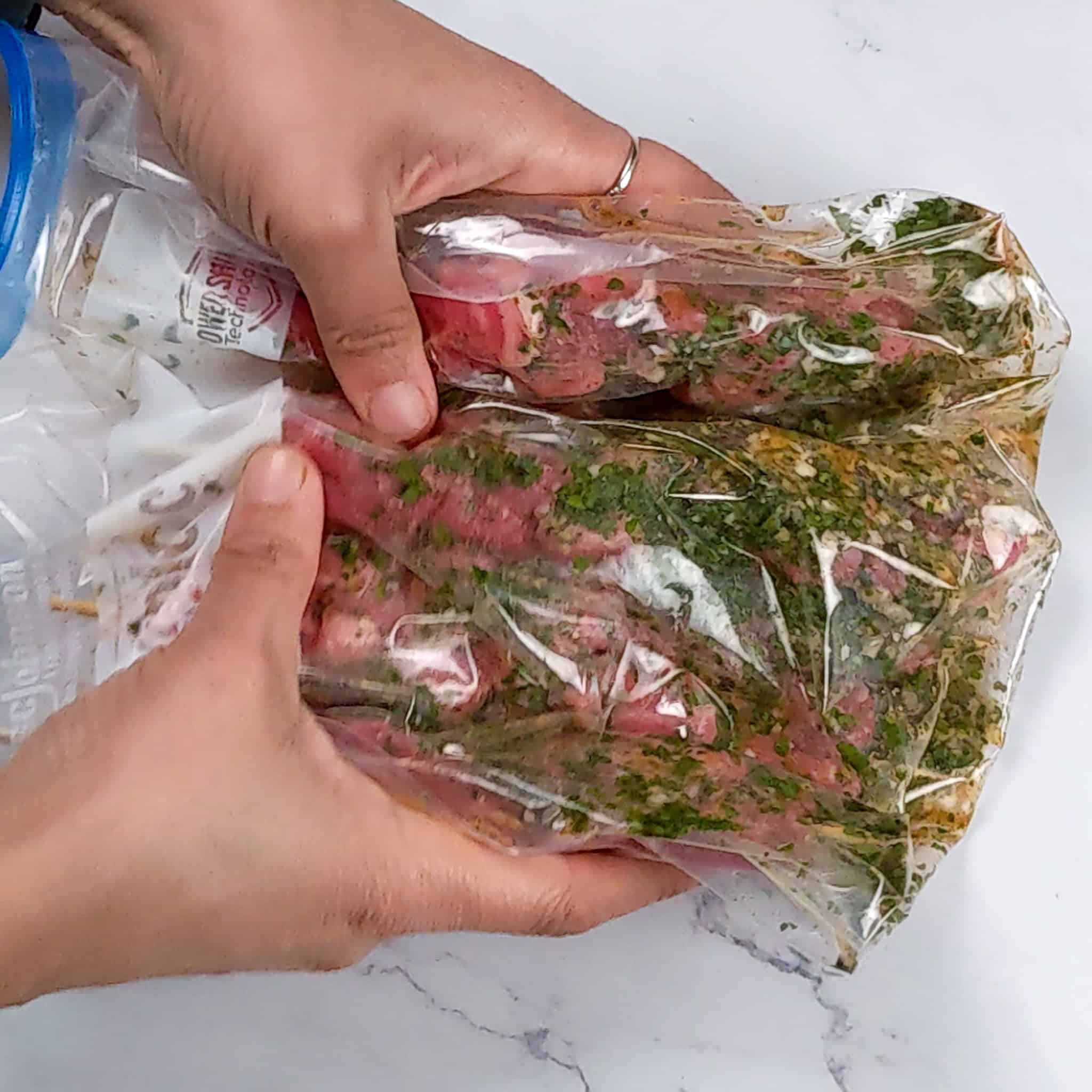 The beef skewers and the marinade in the resealable bag are massaged with two hands.