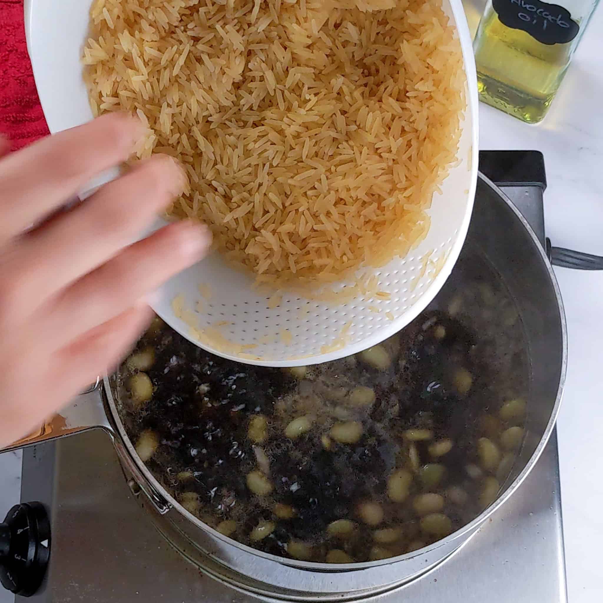 Rinsed and drained parboiled basmati rice in a rice washer being poured into the djon djon black mushroom broth base.