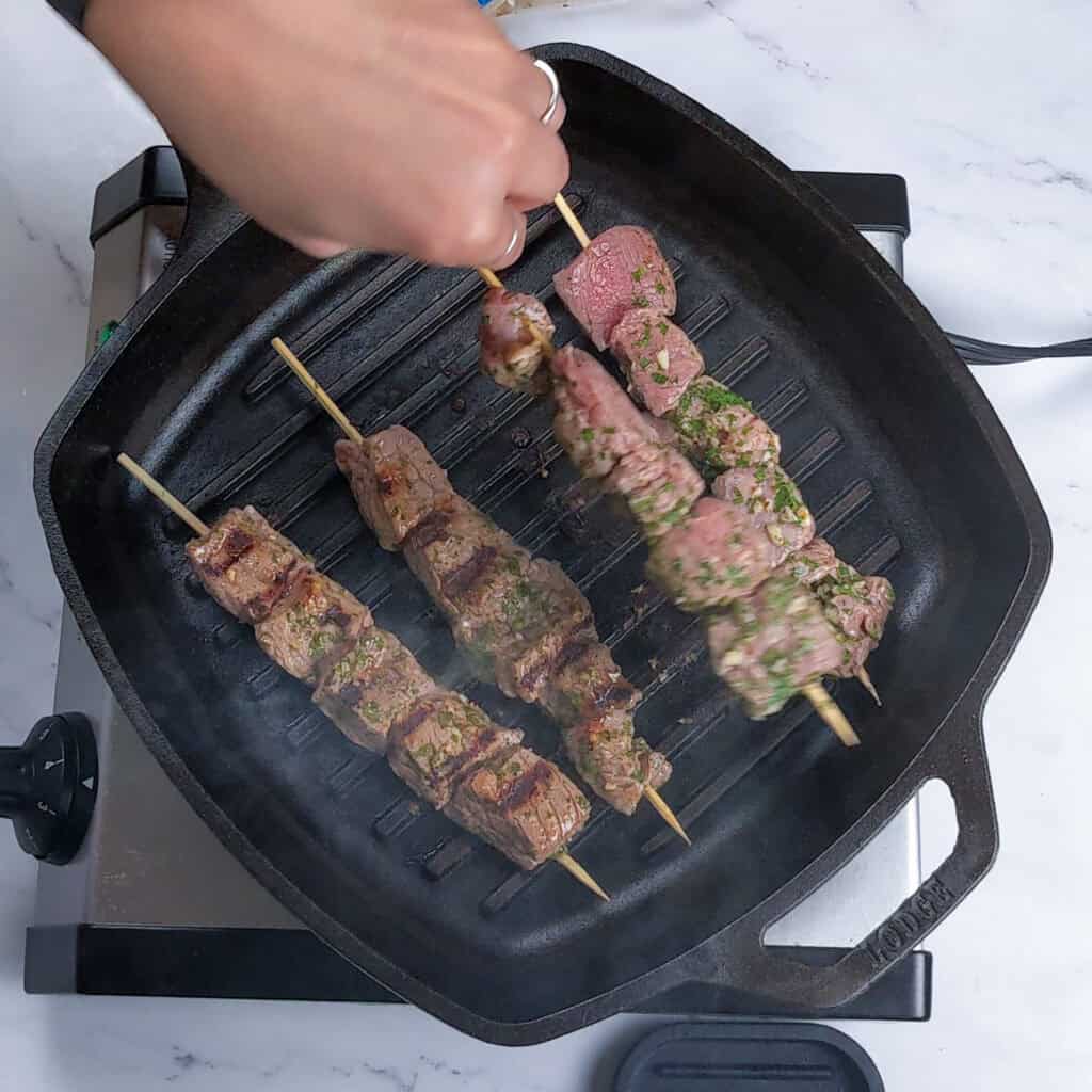 Marinated raw beef skewers grilled in a grill pan.