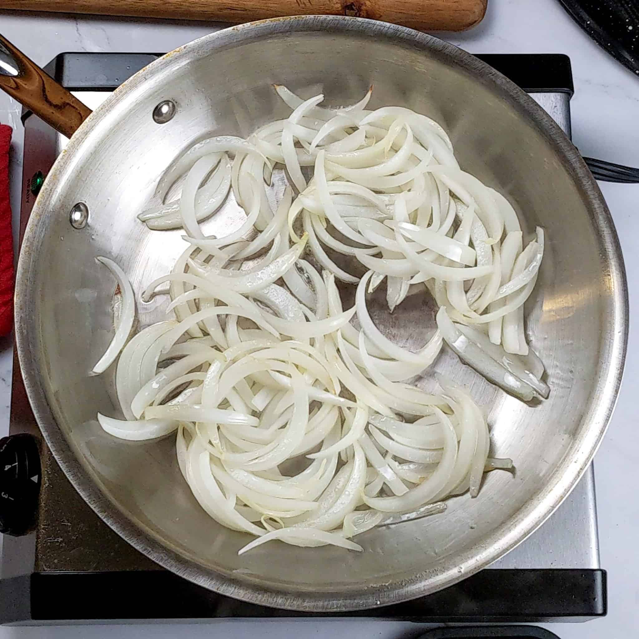 Thinly sliced onions are sauteed in an all-clad stainless steel frying pan.