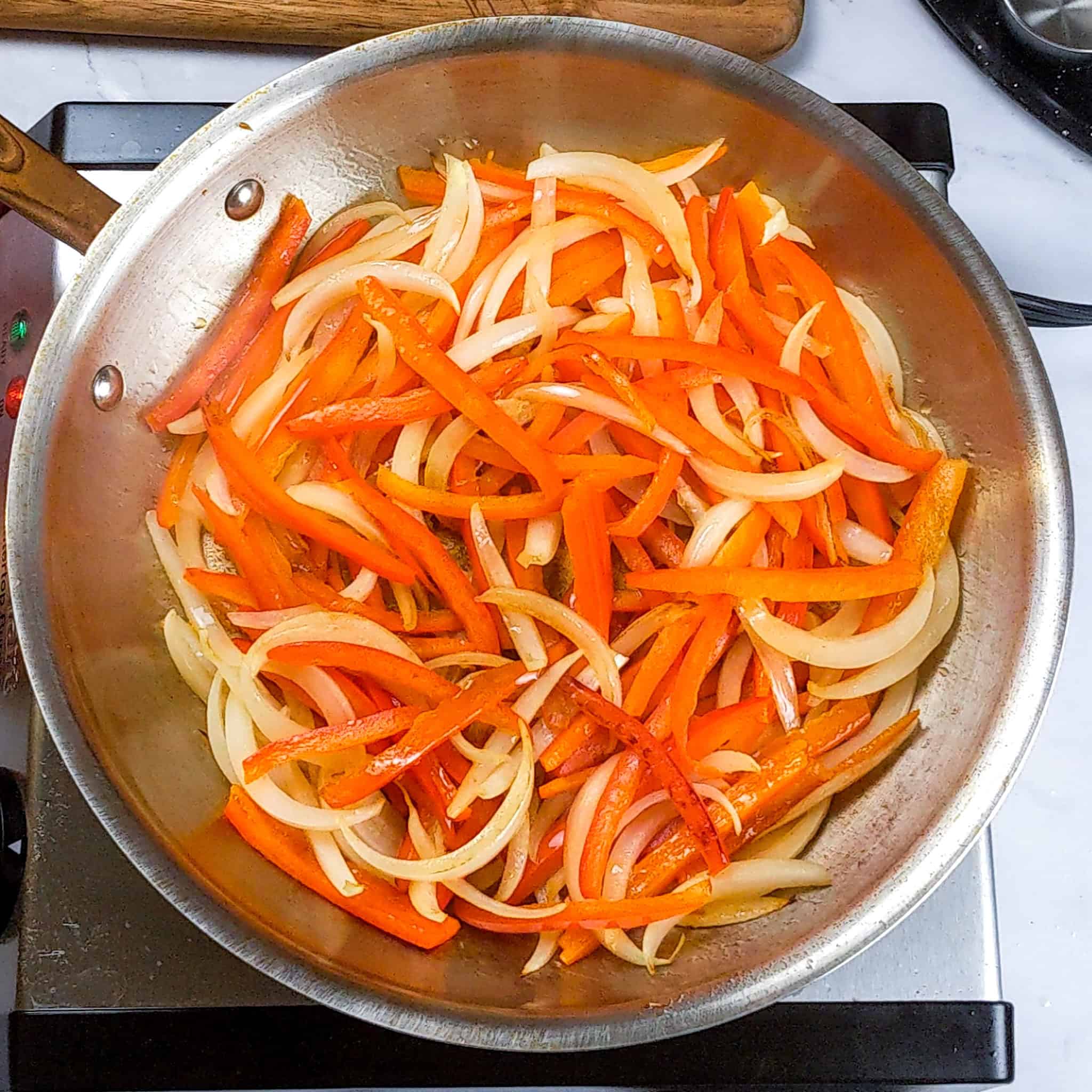 Thinly sliced red bell peppers are added to the onions.