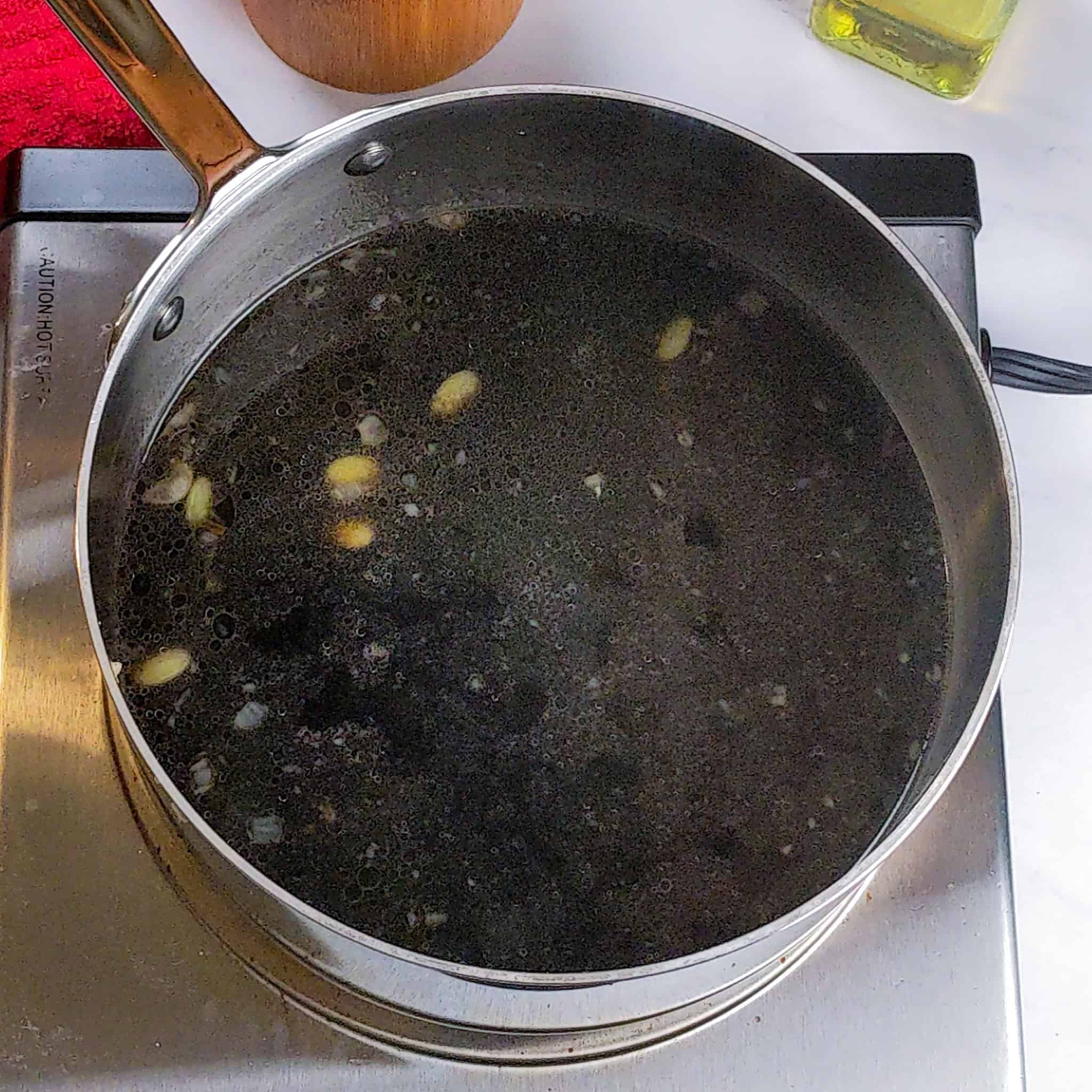 The black mushroom broth in a sauce pot with Lima beans, chopped onions and garlic.