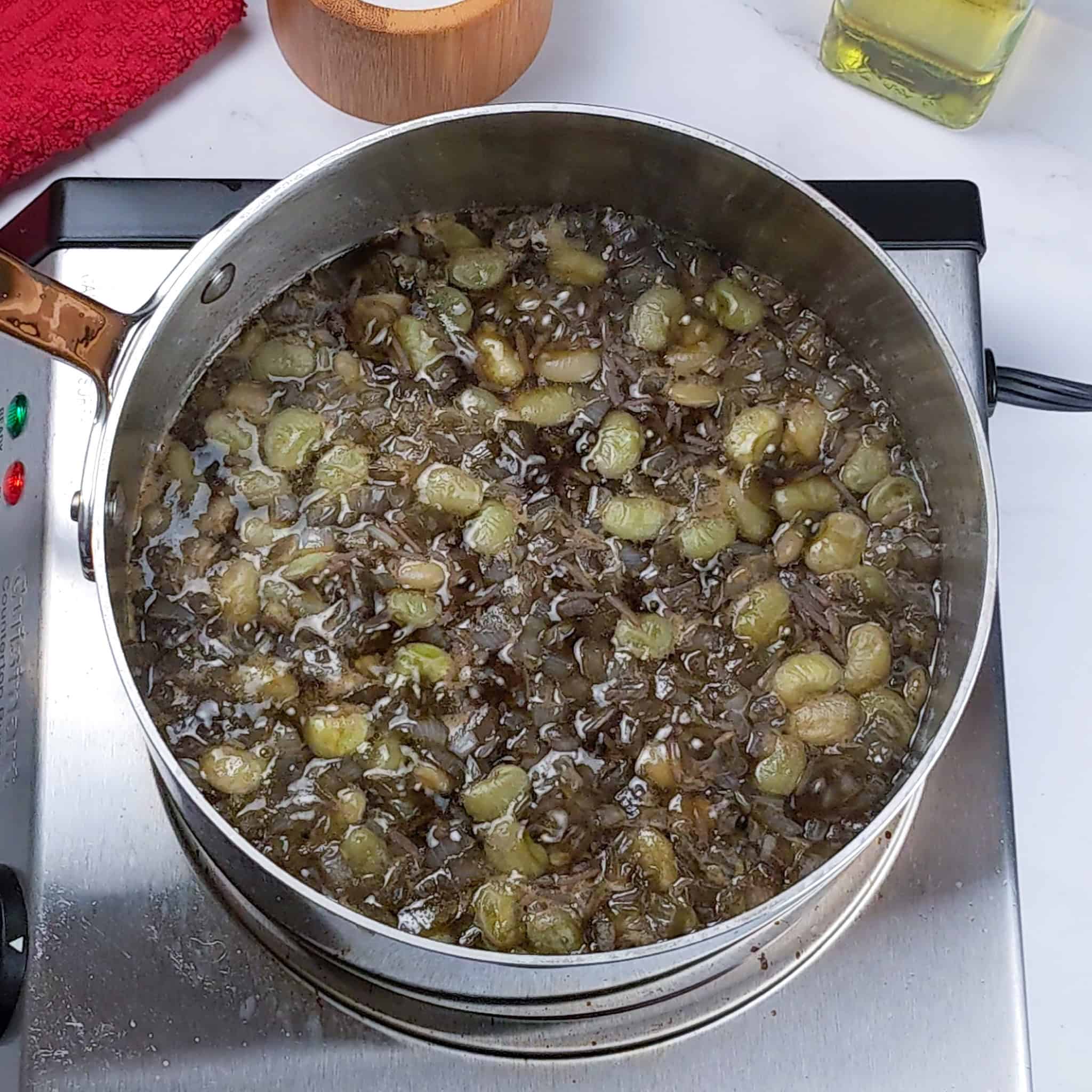 The liquid in the pot is reduced, showing a layer of lima beans, rice, chopped onions, and garlic that has absorbed the djon djon black mushroom broth.