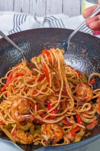 Haitian Styles spaghetti with shrimp in a wok is served with two forks.