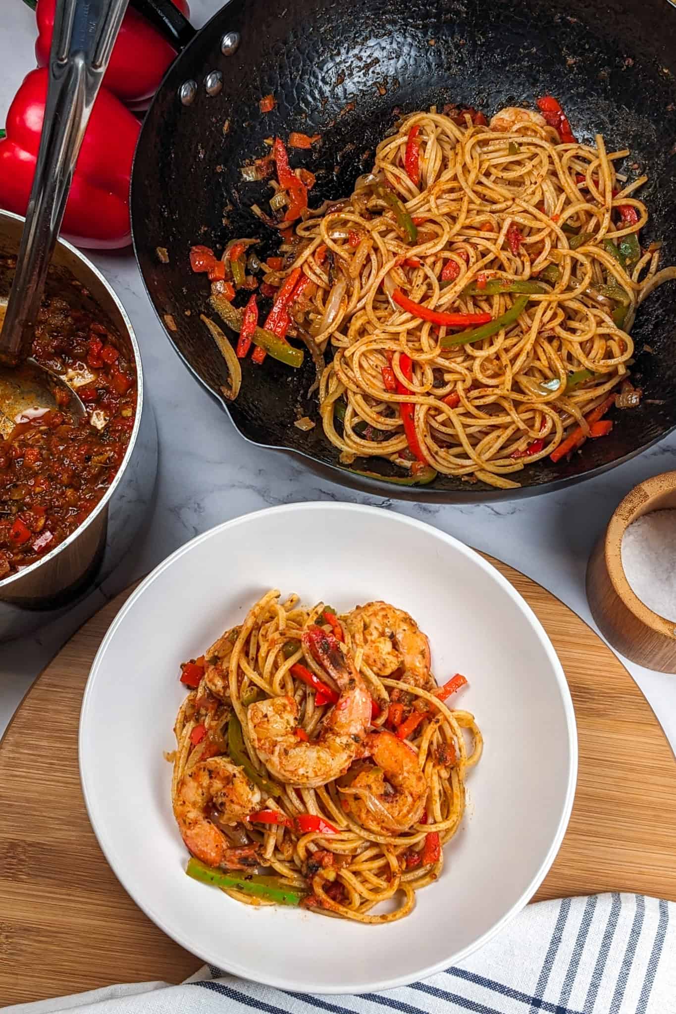 Top view of the Haitian-style spaghetti with shrimp and creole sauce in a wide-rim pasta bowl. Surrounded by more sauce in a saucepan and a wok of pasta.