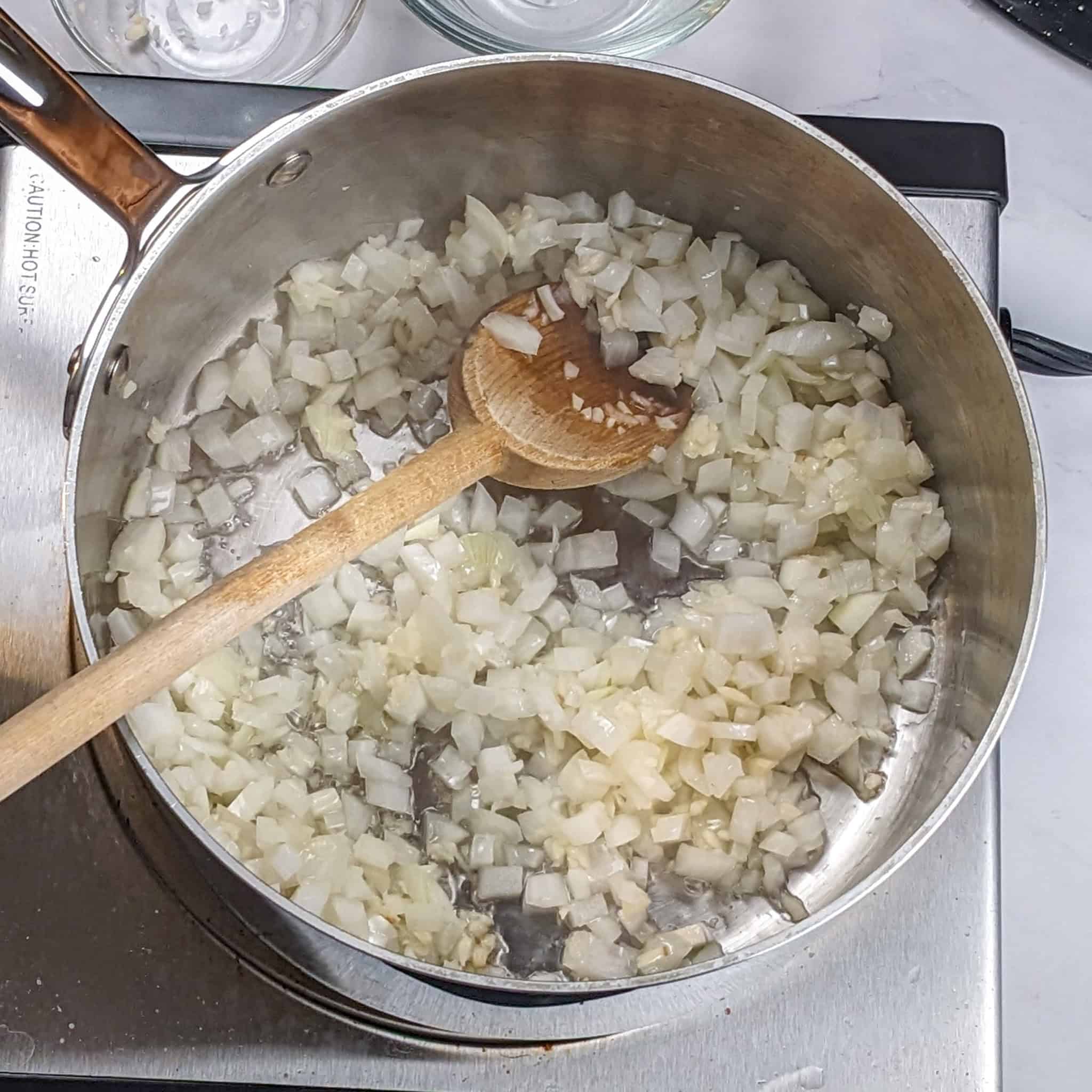 Onion sauteing in a large sauce pot with a wooden spoon.