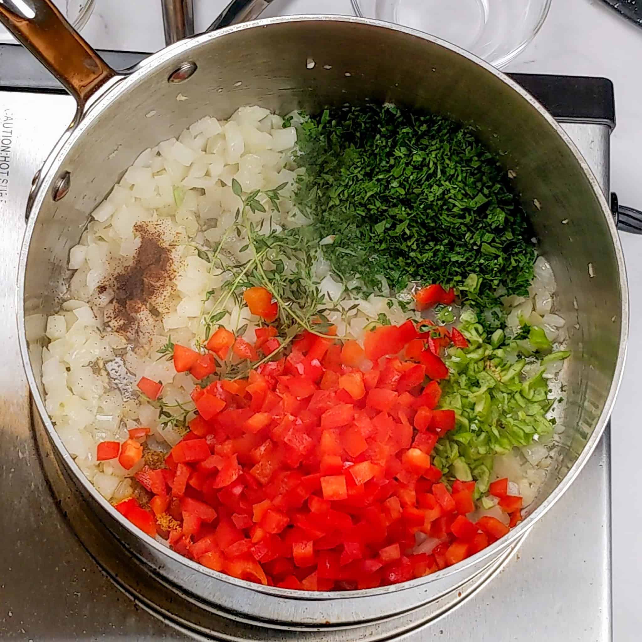 On top of the cooked onions, chopped red bell pepper, Scotch bonnet pepper, fresh thyme, parsley, and ground clove have been added.