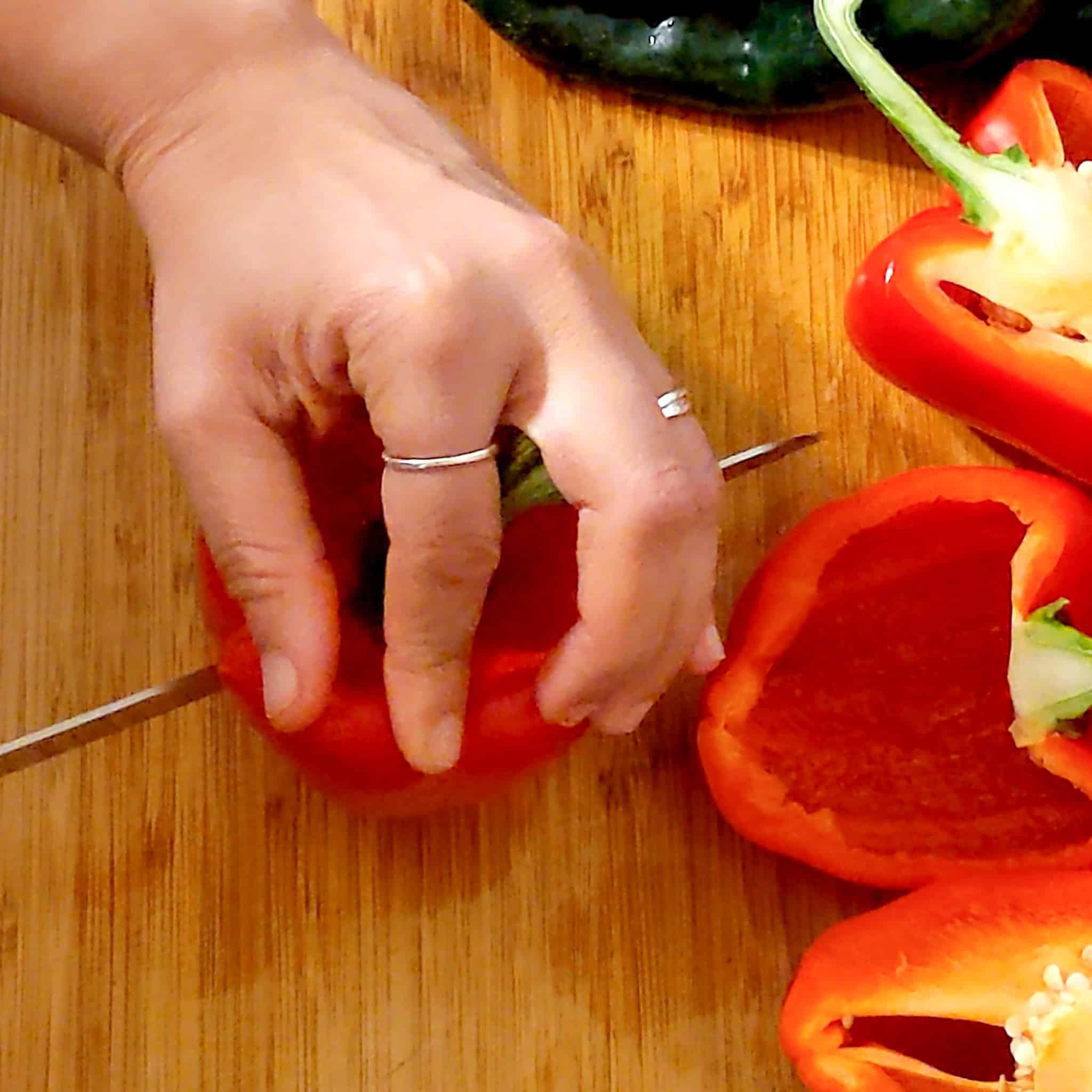 A hand holding the bell pepper at the top while the knife finishes cutting through all the way to the bottom.