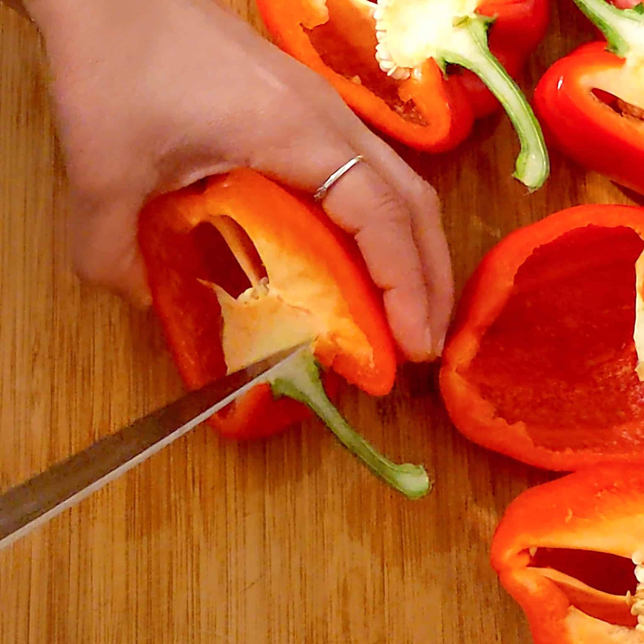 A sharp, pointy knife separates the core from the stem of the halved bell pepper.