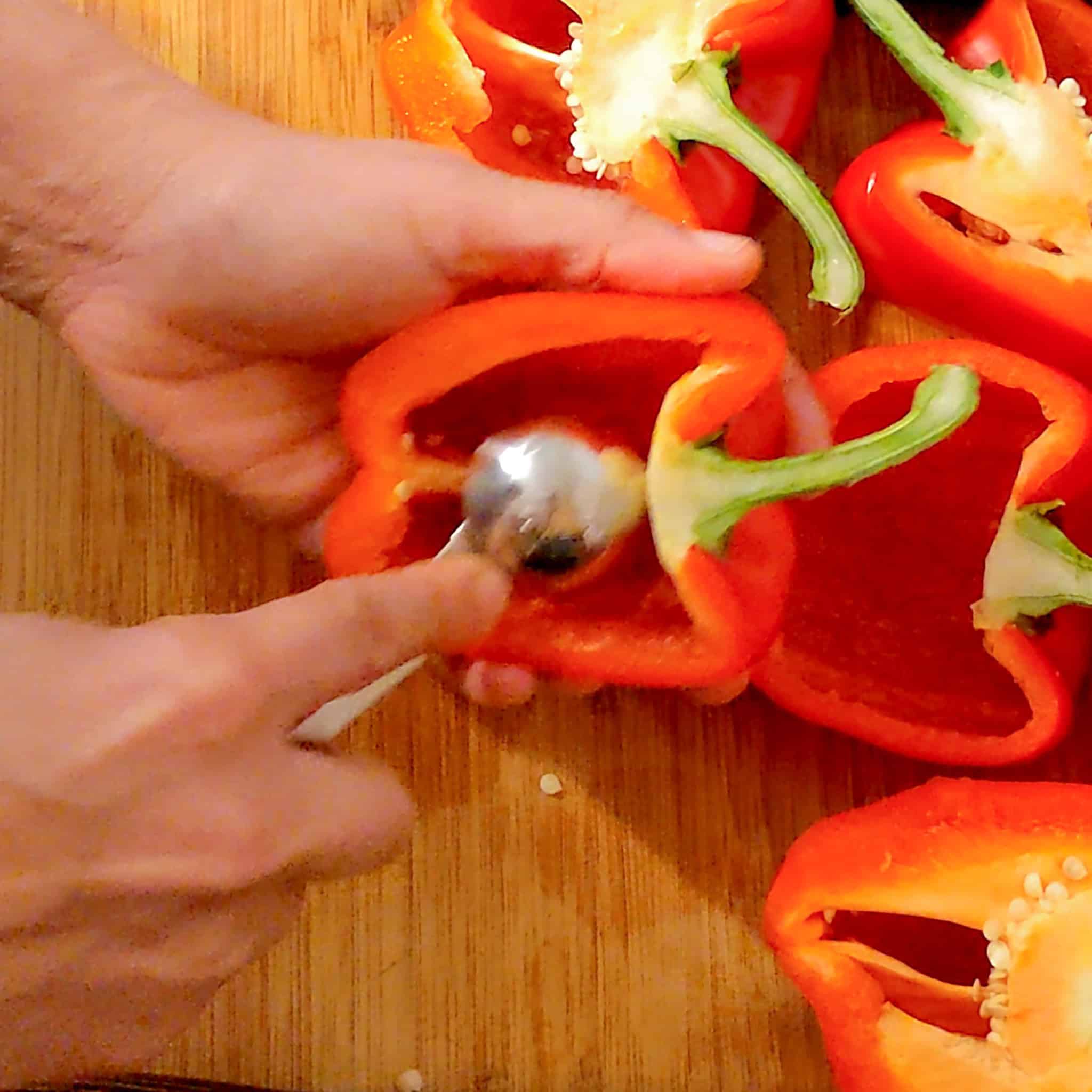 A tablespoon measuring spoon scooping out the rest of the pith in the pepper.