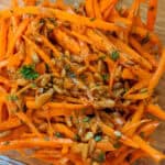 close up of harissa carrot salad of shredded carrots and sunflower seeds and chopped parsley combined with a harissa paste sauce.