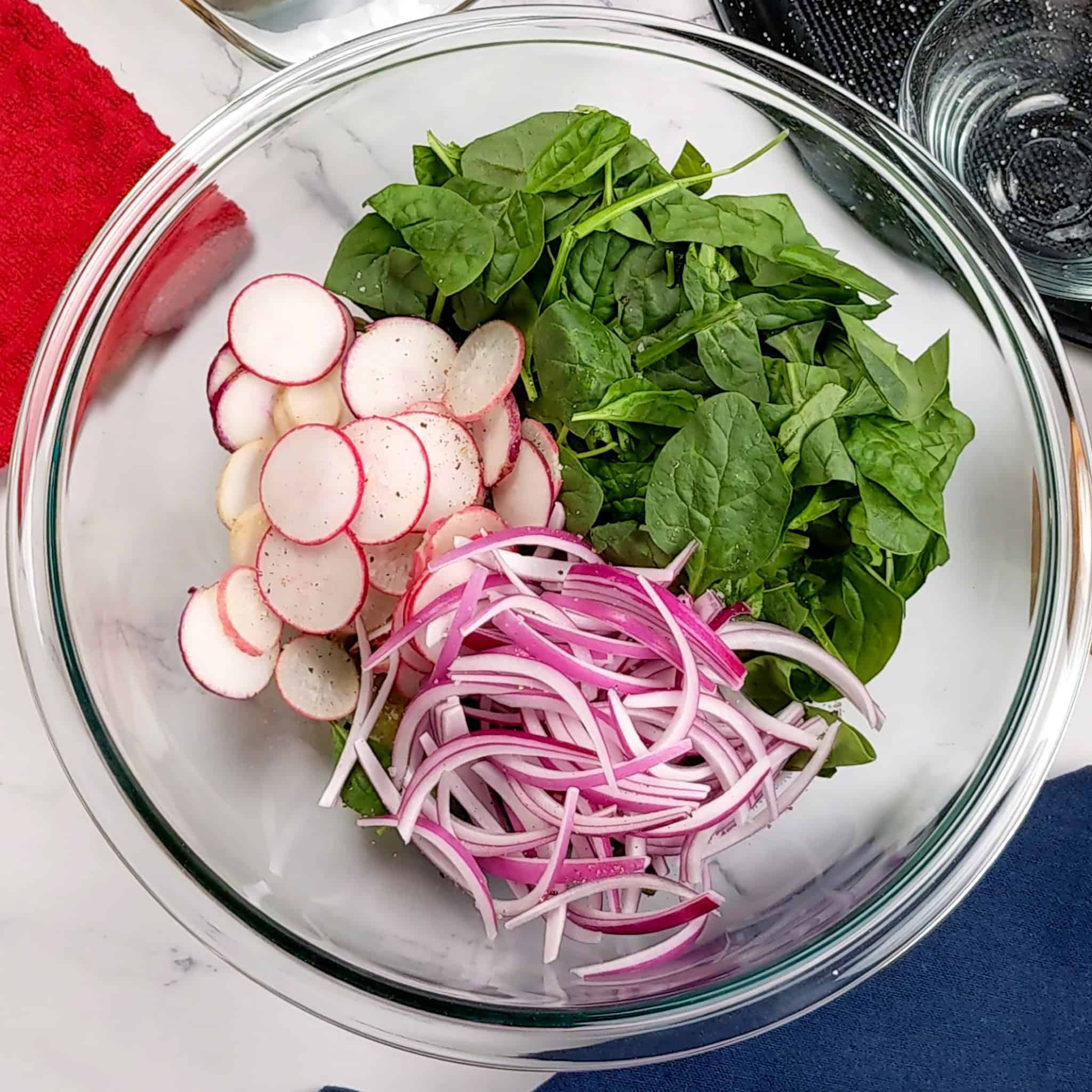 Fresh spinach, tricolor radish, and thinly sliced red onions and a glass mixing bowl.