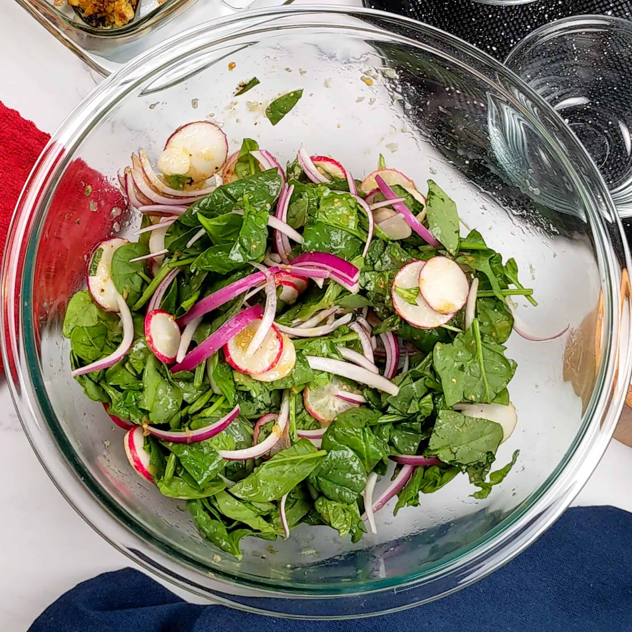 Fresh spinach, tricolor radish, and thinly sliced red onions combined with salsa verde in a glass mixing bowl.