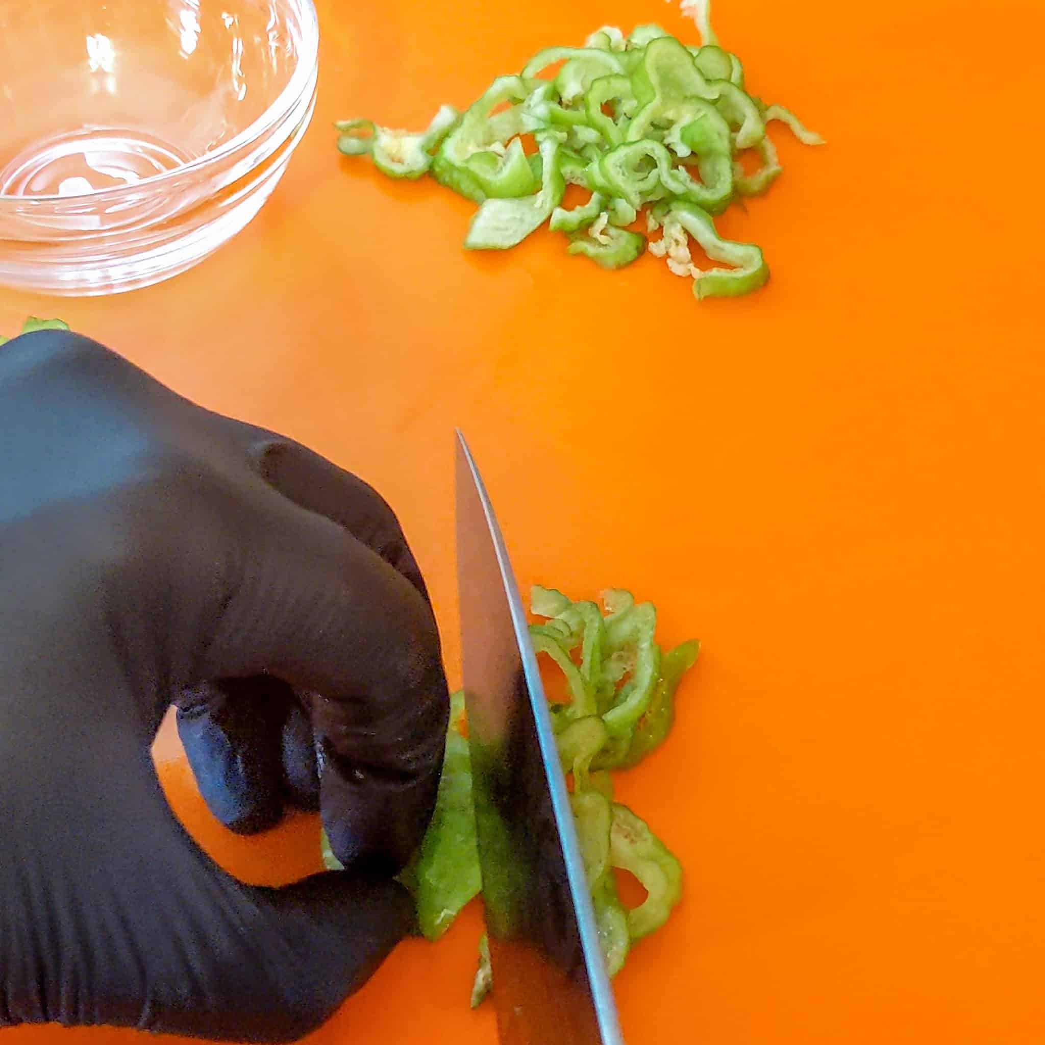 Sharp knife slicing the Scotch bonnet pepper Into Thin strips.