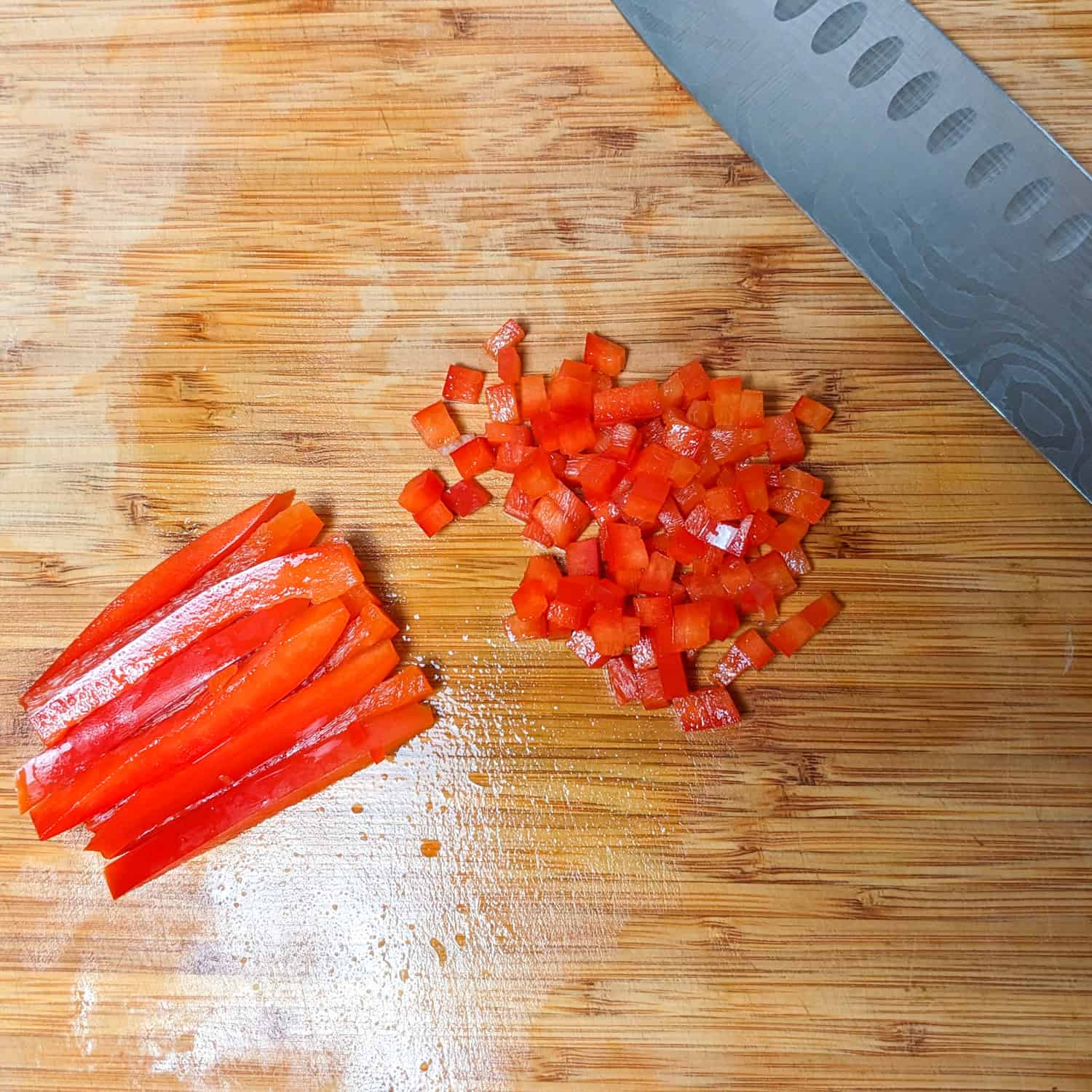 sliced bell peppers and small diced bell peppers on a cutting board with a knife.