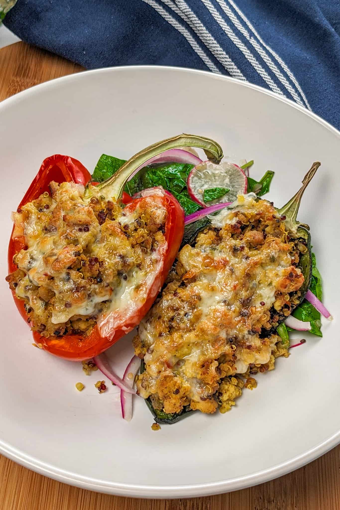 Baked stuffed bell peppers and poblano peppers with ground turkey and quinoa with melted pepper jack cheese on a bed of greens with sliced radishes and red onion.