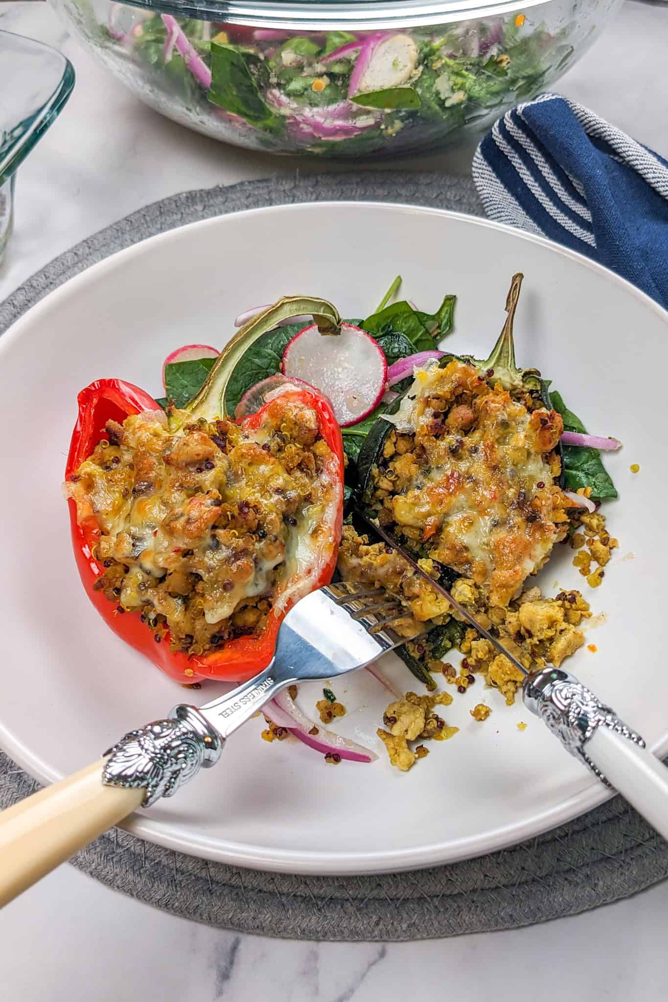 The spicy ground turkey stuffed peppers with salad being eaten with a fork and a knife.