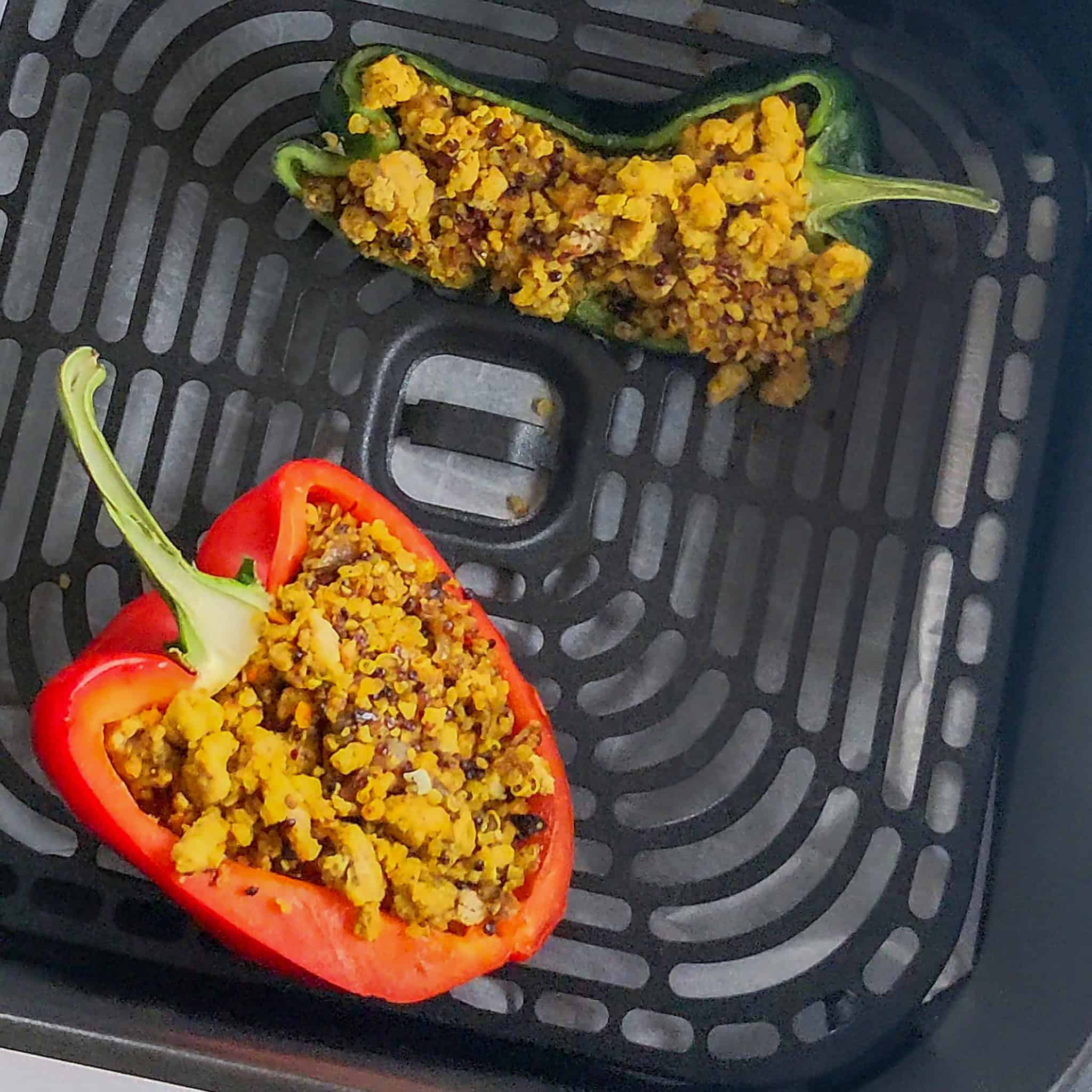 Stuffed bell pepper and poblano pepper laying in an air fryer basket.