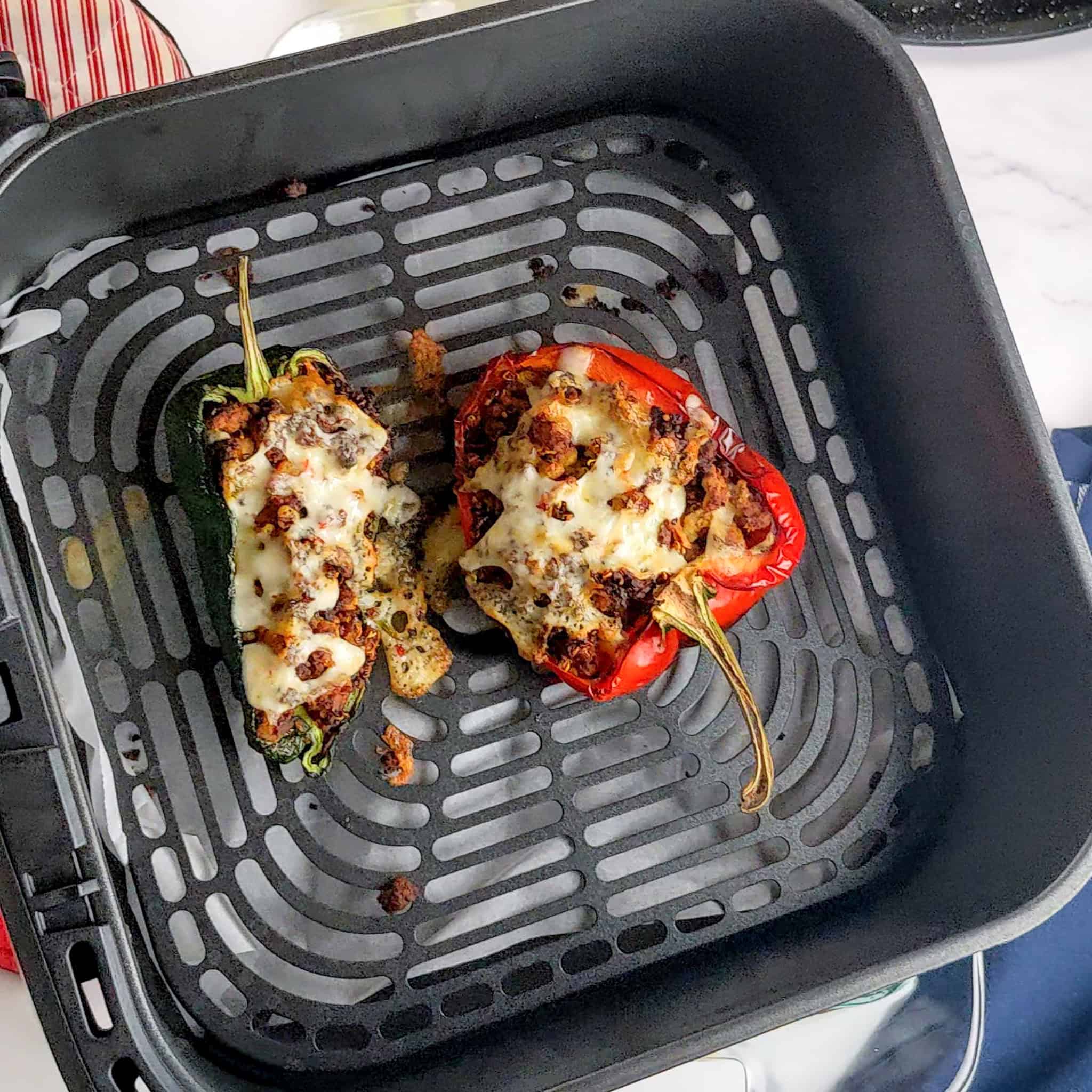 Air-fried stuffed poblano and bell pepper with melted pepper jack cheese in an air fryer basket.