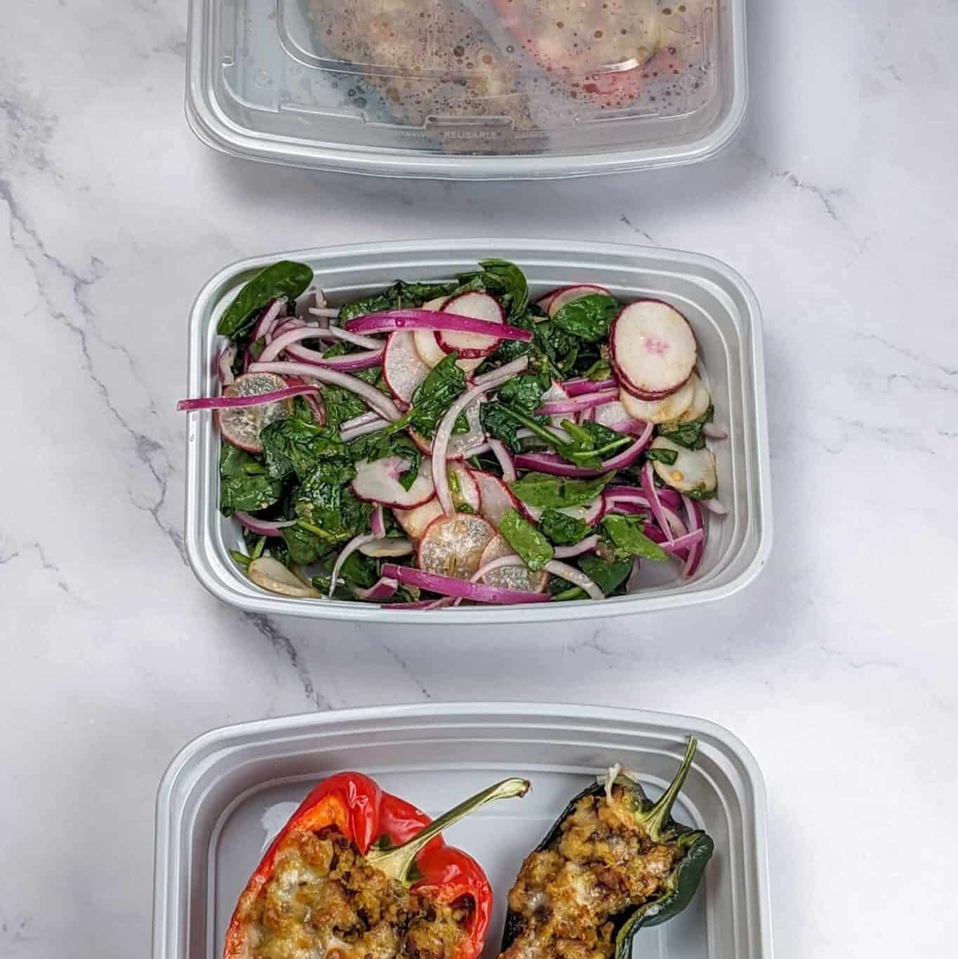 The spicy ground turkey stuffed peppers and salad in separate meal prep containers.