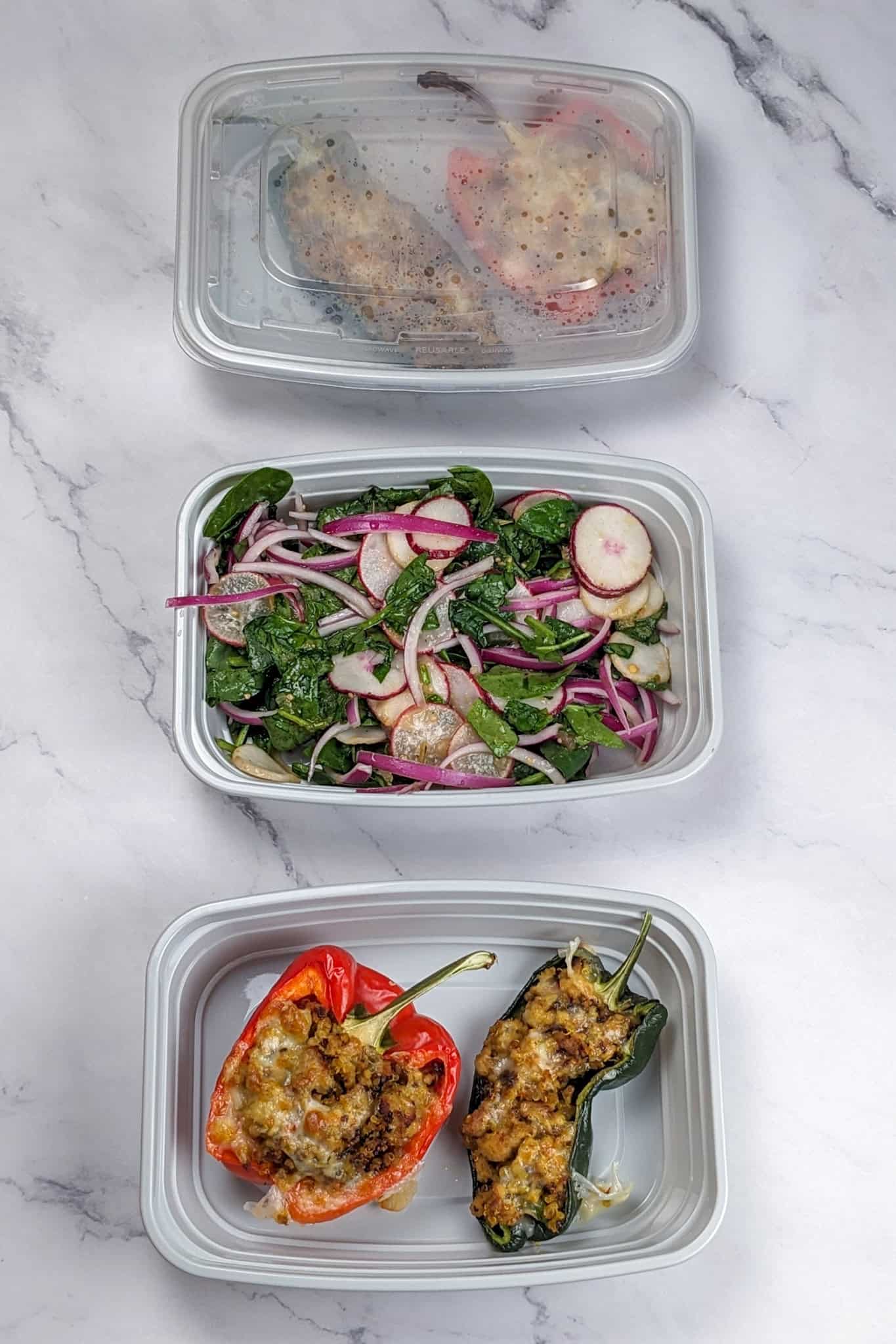 The spicy ground turkey stuffed peppers and salad in separate meal prep containers.